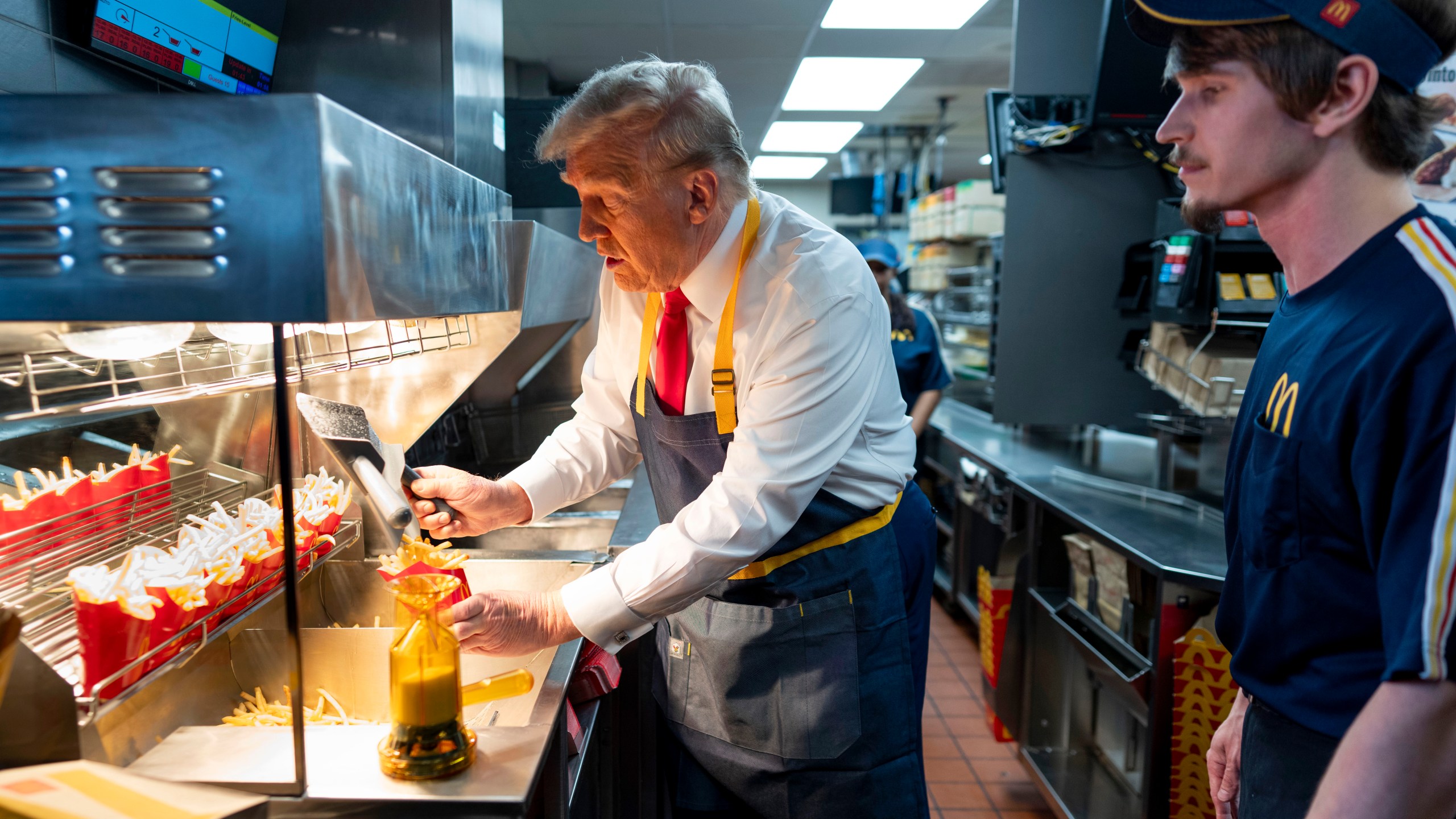 Republican presidential nominee former President Donald Trump, left, uses a frier as an employee looks on during a visit to McDonald's in Feasterville-Trevose, Pa., Sunday, Oct. 20, 2024. (Doug Mills/The New York Times via AP, Pool)