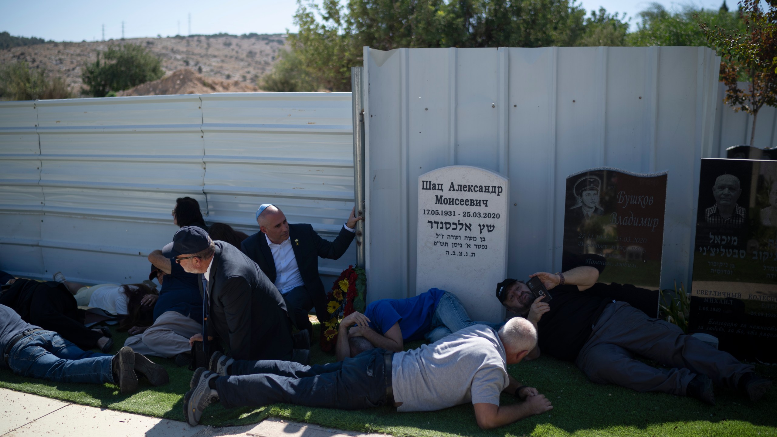 People take cover as a siren warns of incoming rockets during the funeral of Alexei Popov, who was killed during a rocket attack fired from Lebanon last weekend, at the Tel Regev cemetery in the outskirts of Haifa, northern Israel, Monday, Oct. 21, 2024. (AP Photo/Leo Correa)