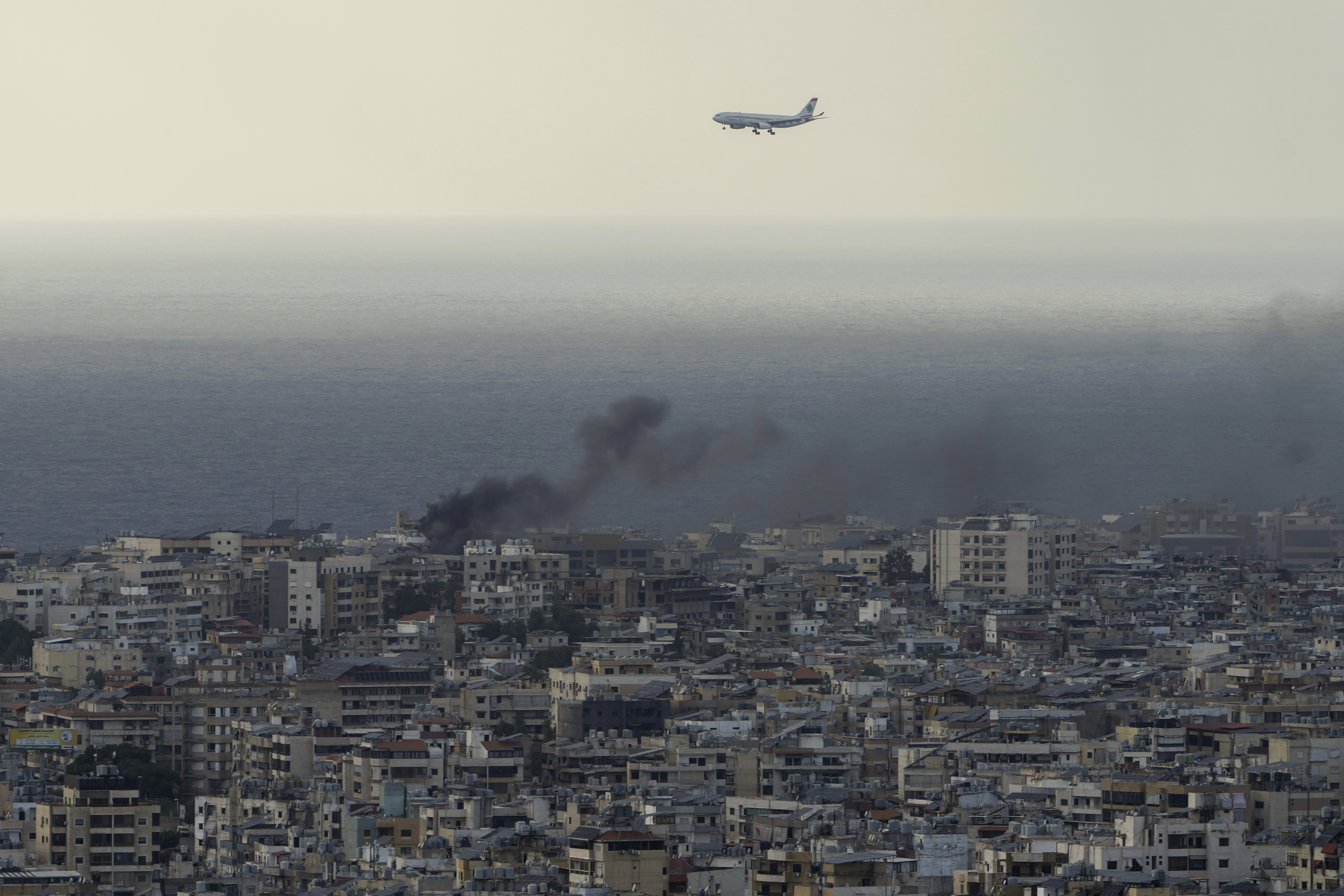 A Middle East Airlines airplane flies over Beirut as smoke rises from Israeli airstrikes in Dahiyeh, Beirut, Tuesday, Oct. 1, 2024. (AP Photo/Bilal Hussein)