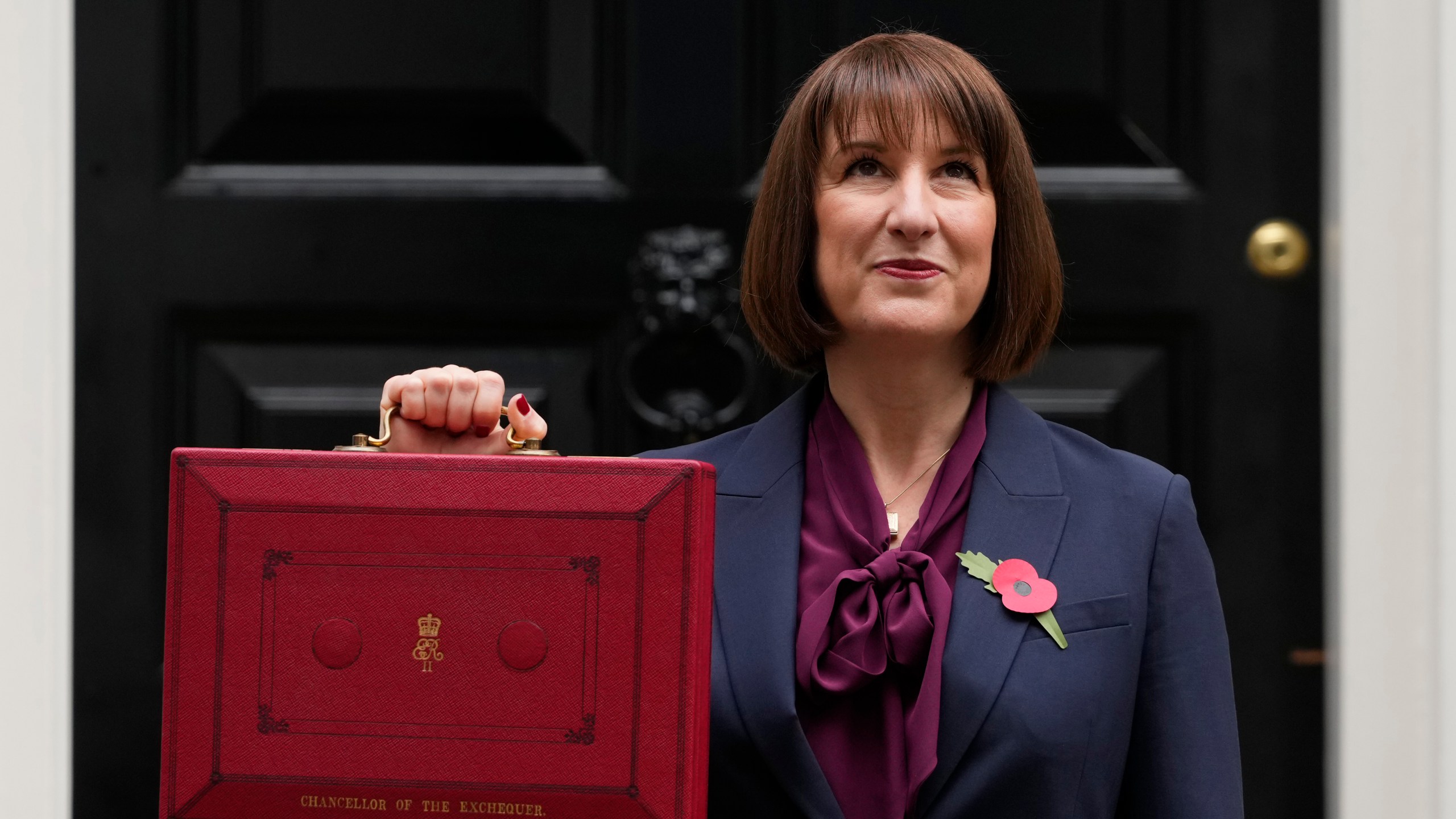 Britain's Chancellor of the Exchequer, Rachel Reeves, looks up as she holds up the traditional red ministerial box containing her budget speech, as she poses for the media outside No 11 Downing Street, before departing to the House of Commons to deliver the budget in London, Wednesday, Oct. 30, 2024. (AP Photo/Kirsty Wigglesworth)