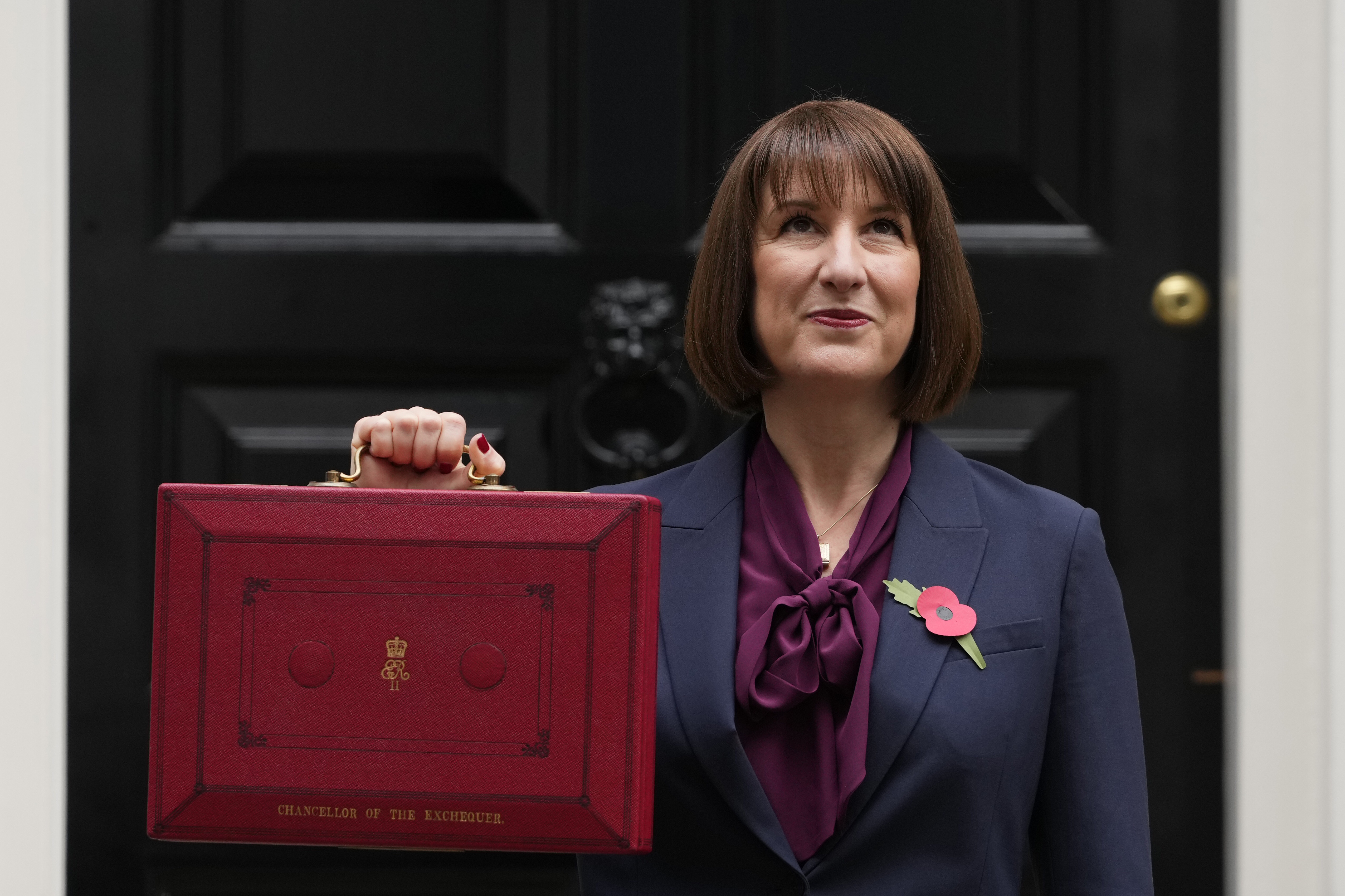 Britain's Chancellor of the Exchequer, Rachel Reeves, looks up as she holds up the traditional red ministerial box containing her budget speech, as she poses for the media outside No 11 Downing Street, before departing to the House of Commons to deliver the budget in London, Wednesday, Oct. 30, 2024. (AP Photo/Kirsty Wigglesworth)