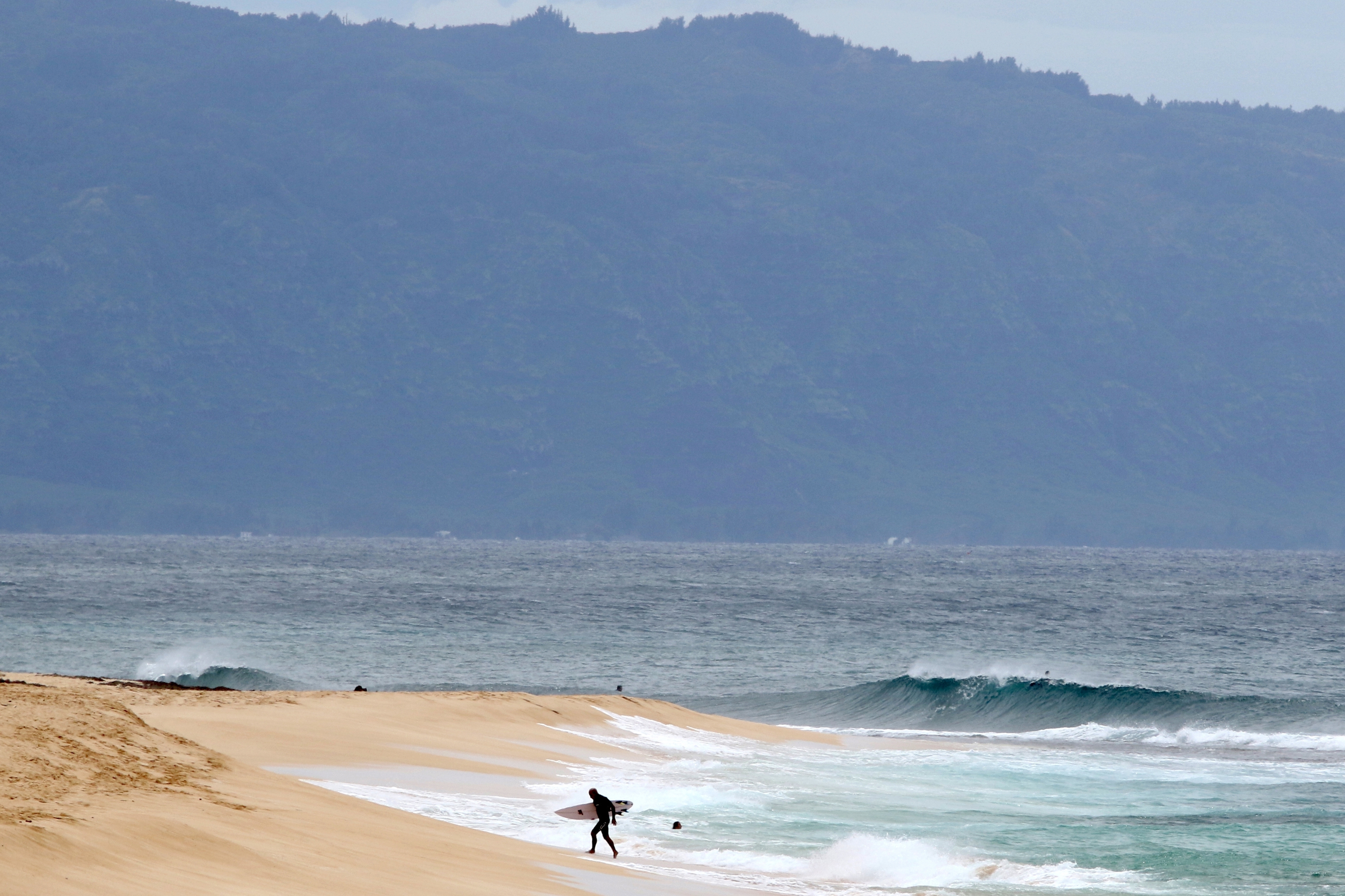 FILE - A surfer walks out of the ocean on Oahu's North Shore near Haleiwa, Hawaii, March 31, 2020. (AP Photo/Caleb Jones, File)