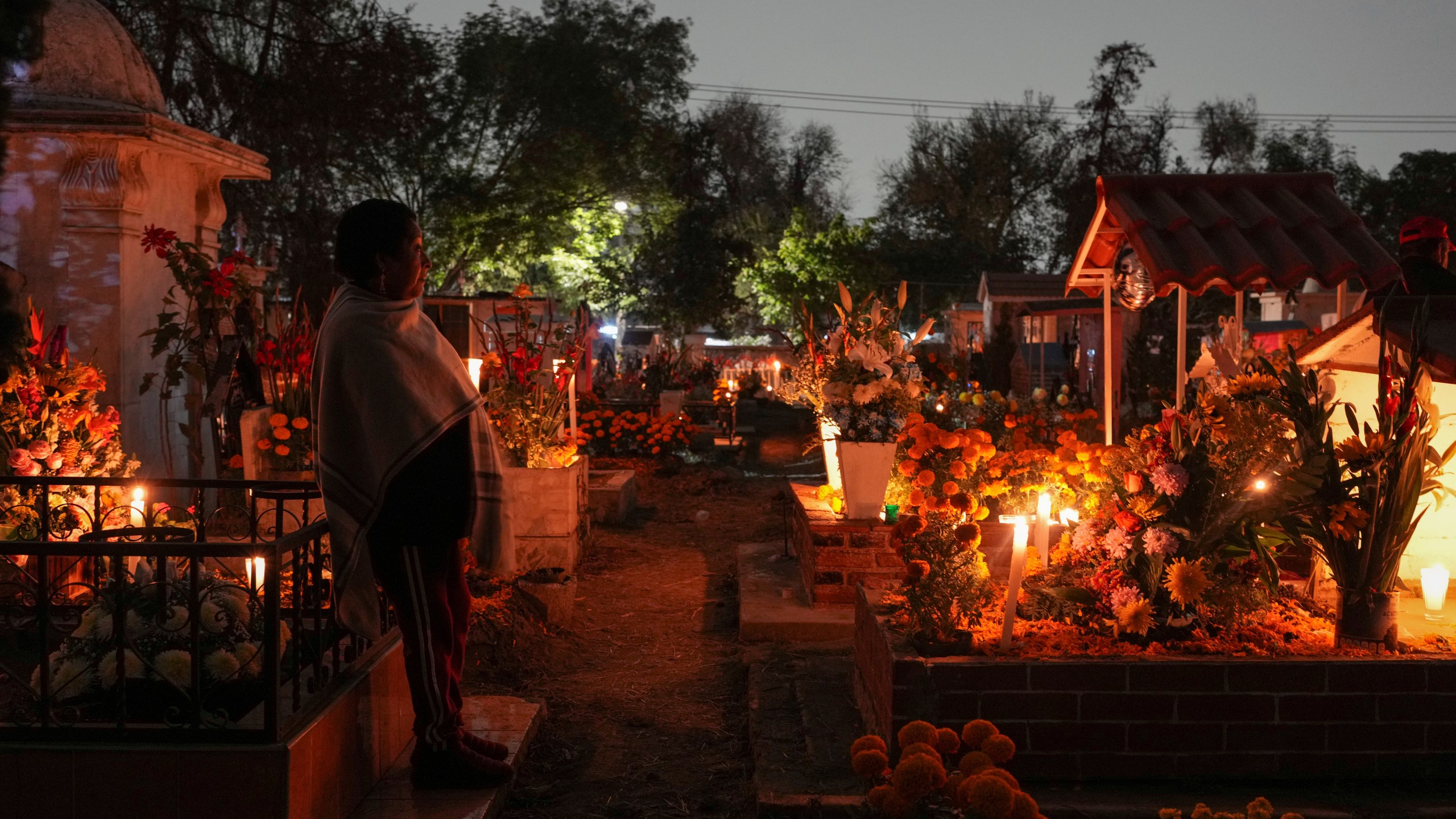 A woman stands at a tomb of a dearly departed, celebrating Day of the Dead, at the San Gregorio Atlapulco cemetery on the outskirts of Mexico City, Friday, Nov. 1, 2024. (AP Photo/Moises Castillo)