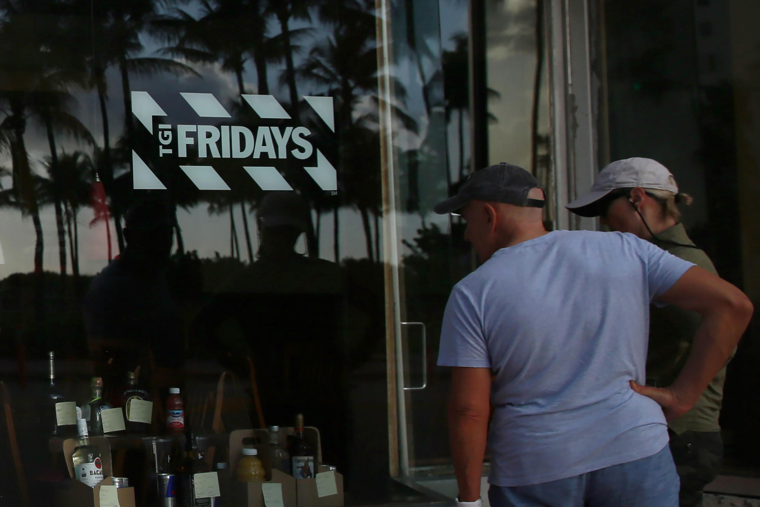 FILE - People peek into a window of a TGI Friday's restaurant to see what they are serving to-go on Wednesday, March 25, 2020, in Miami Beach, Fla. (AP Photo/Brynn Anderson, File)