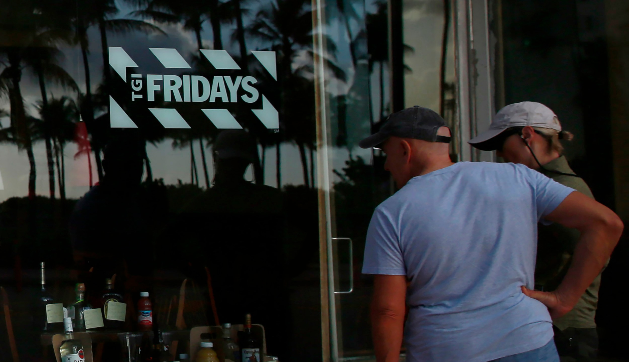 FILE - People peek into a window of a TGI Friday's restaurant to see what they are serving to-go on Wednesday, March 25, 2020, in Miami Beach, Fla. (AP Photo/Brynn Anderson, File)