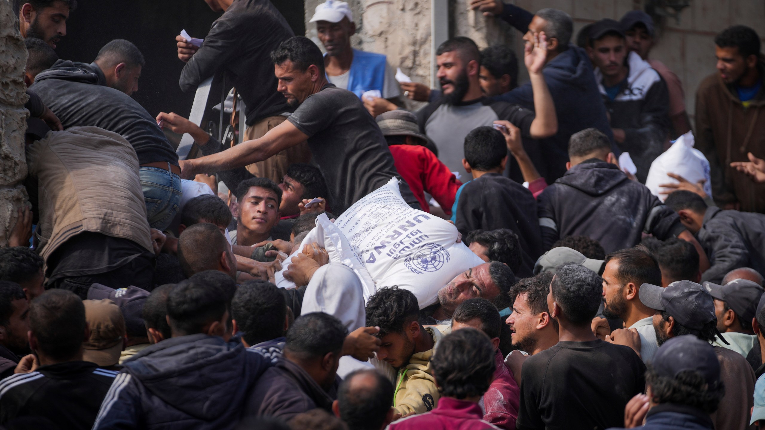 Palestinians gather to receive bags of flour distributed by UNRWA, the U.N. agency helping Palestinian refugees, in Deir al Balah, central Gaza Strip, Saturday, Nov. 2, 2024. (AP Photo/Abdel Kareem Hana)