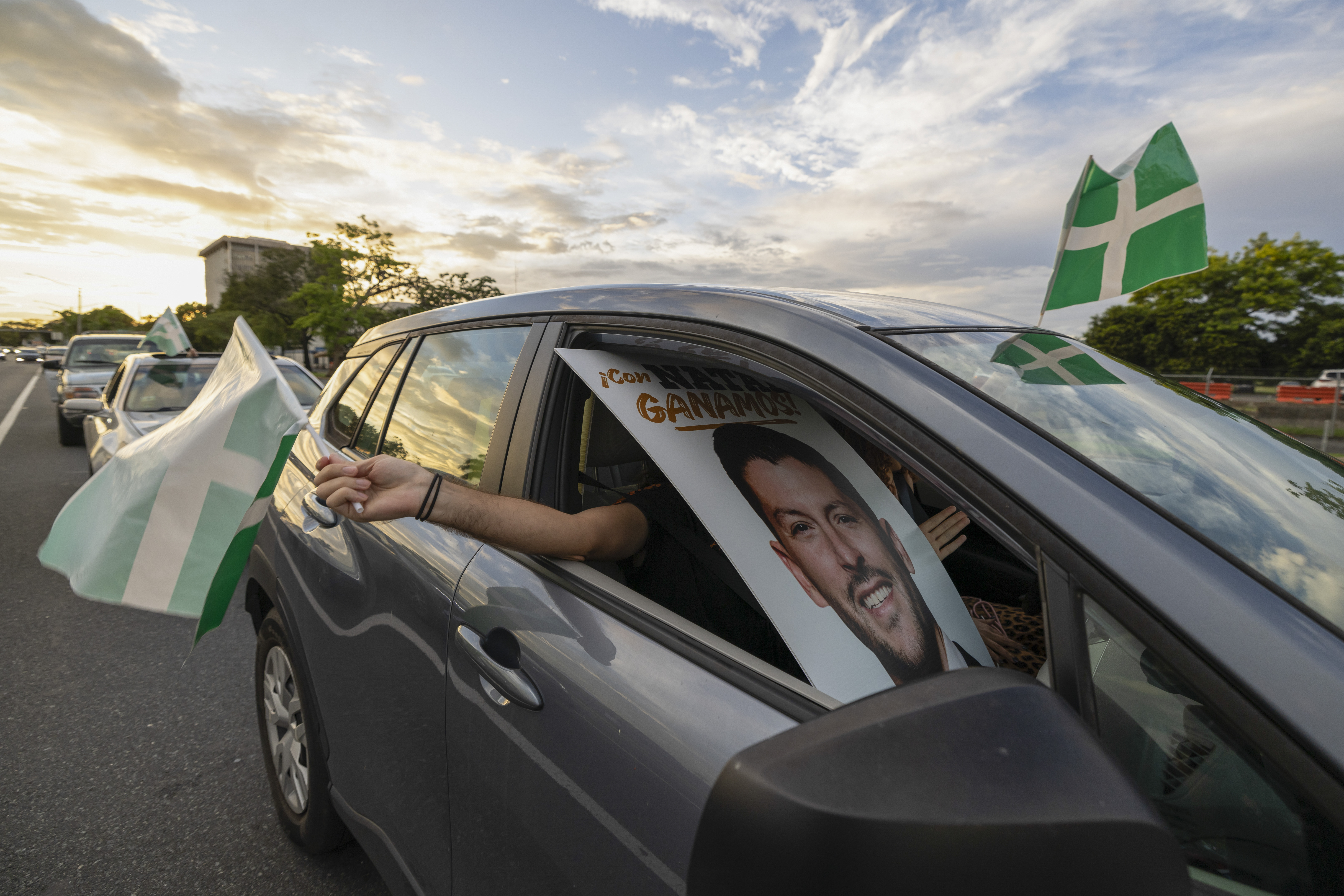 A supporter waves a Puerto Rican Independence Party flag while holding a campaign poster promoting the Citizens' Victory Movement mayoral candidate Manuel Natal, during a caravan in San Juan, Puerto Rico, Friday, Nov. 1, 2024. (AP Photo/Alejandro Granadillo)