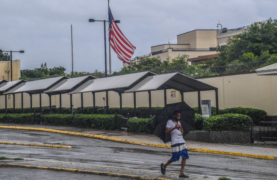 A man walks past the the U.S. Embassy during rains brought on by tropical storm Rafael in Kingston, Jamaica, Tuesday, Nov. 5, 2024. (AP Photo/Collin Reid)