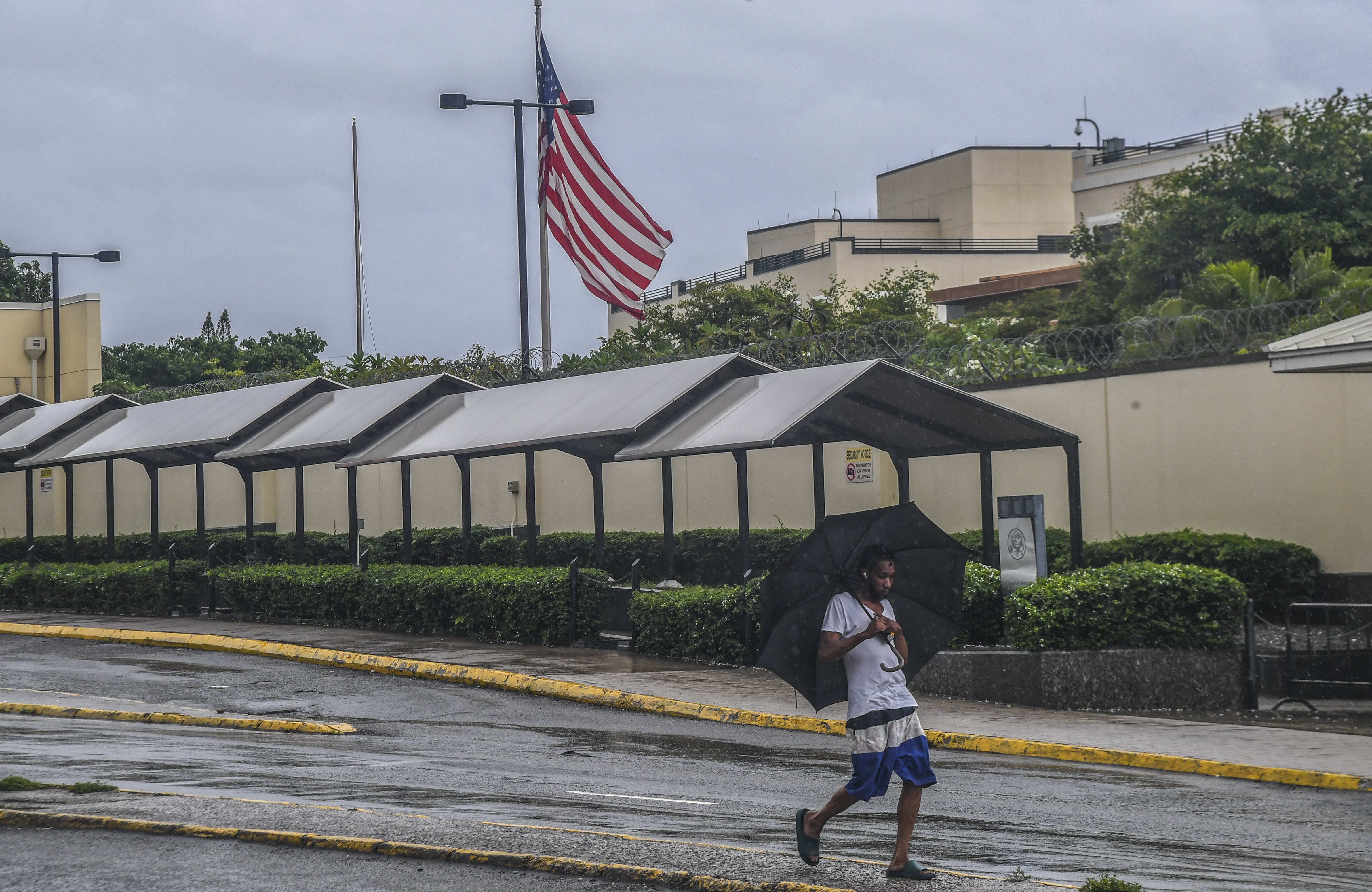 A man walks past the the U.S. Embassy during rains brought on by tropical storm Rafael in Kingston, Jamaica, Tuesday, Nov. 5, 2024. (AP Photo/Collin Reid)