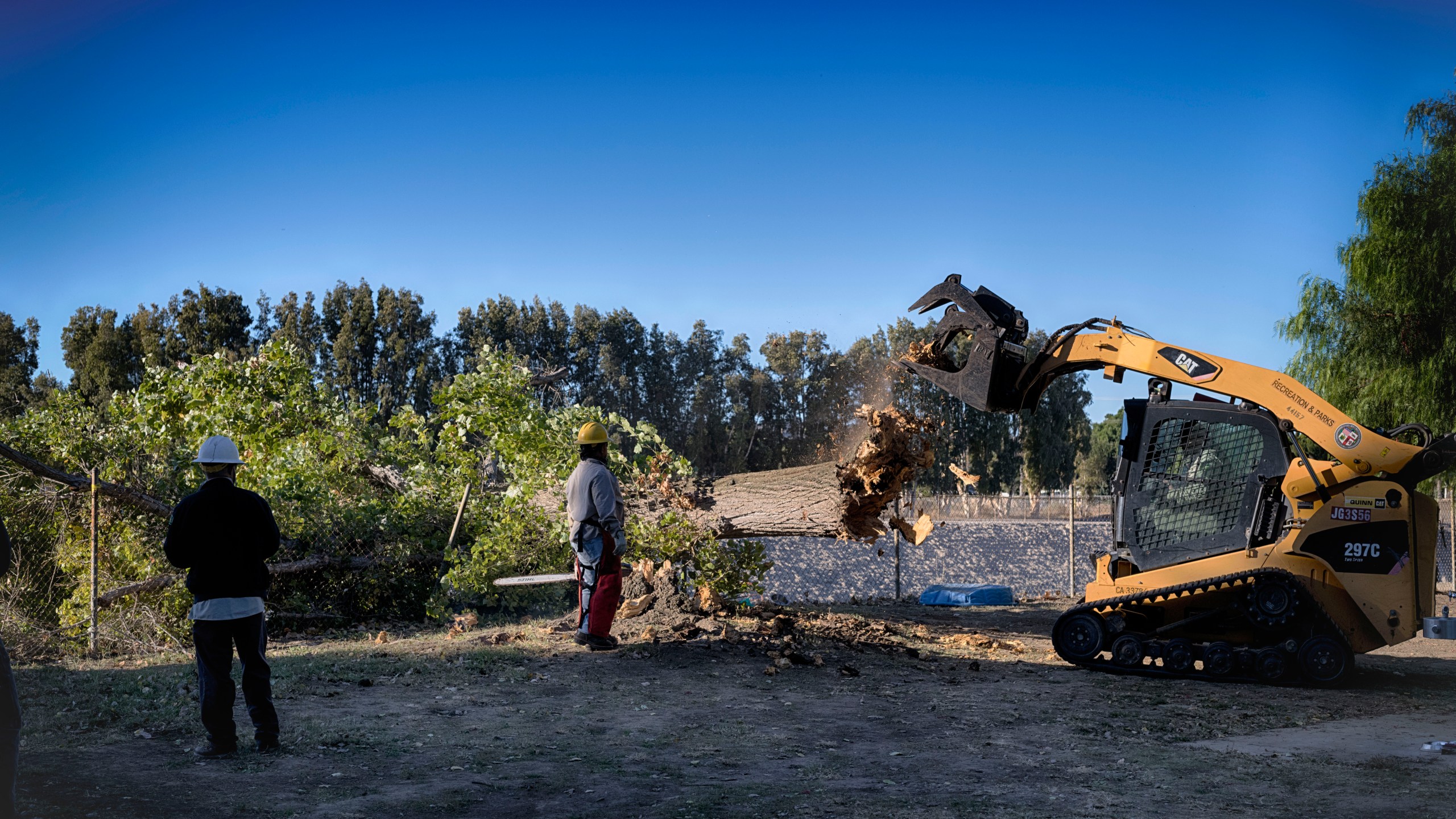 Los Angeles city workers remove the remains of a fallen tree blown over by intense winds that crushed a fence in a city park on Monday, Nov. 4, 2024. (AP Photo/Richard Vogel)