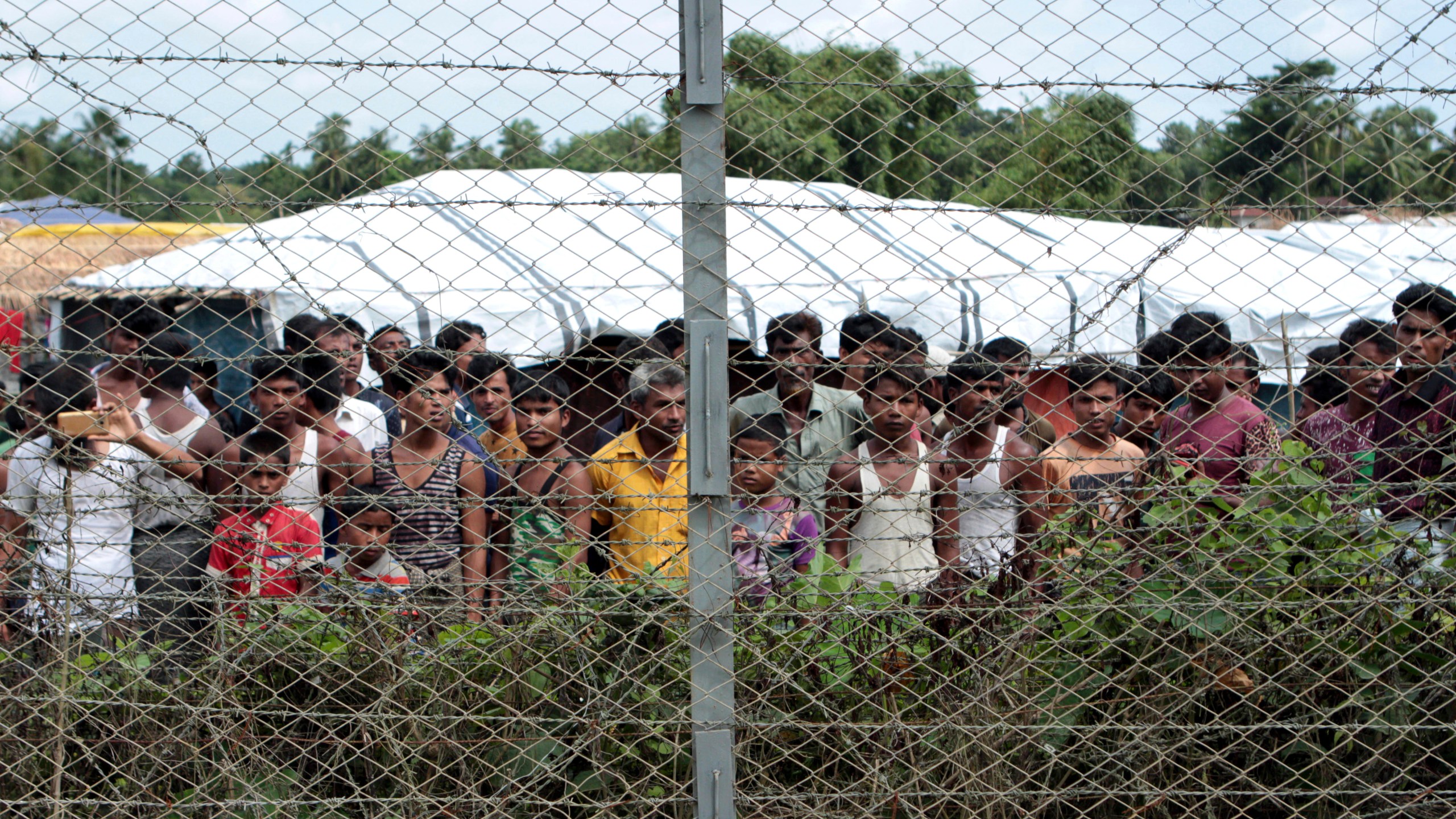 FILE - Rohingya refugees gather near a fence during a government organized media tour, to a no-man's land between Myanmar and Bangladesh, near Taungpyolatyar village, Maung Daw, northern Rakhine State, Myanmar, June 29, 2018. (AP Photo/Min Kyi Thein, File)