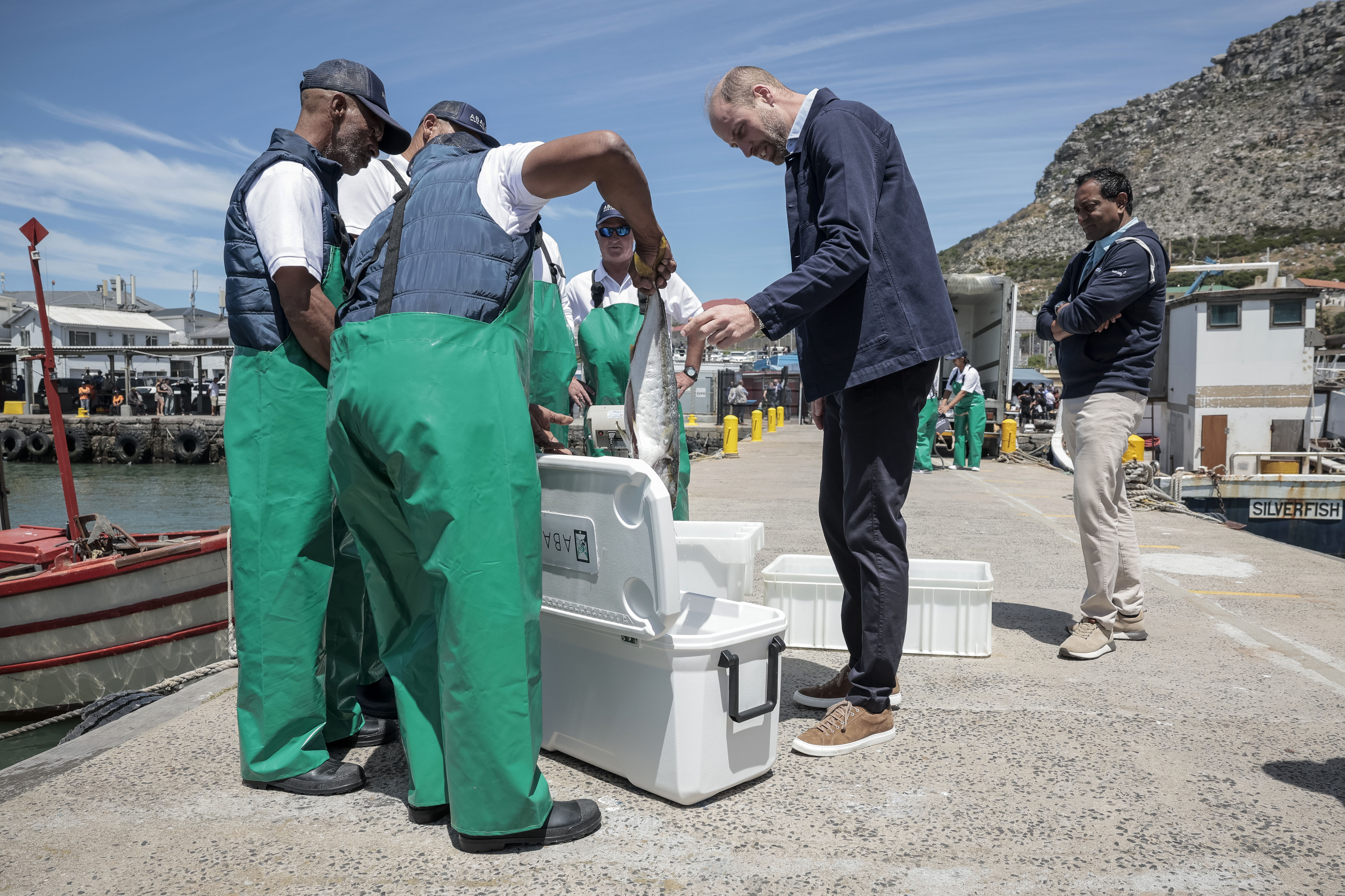 Britain's Prince William, the Prince of Wales is handed a fish as he speaks to local fisherman, at Kalk Bay Harbour, near Cape Town, Thursday, Nov. 7, 2024. (Gianluigi Guercia/Pool Photo via AP)