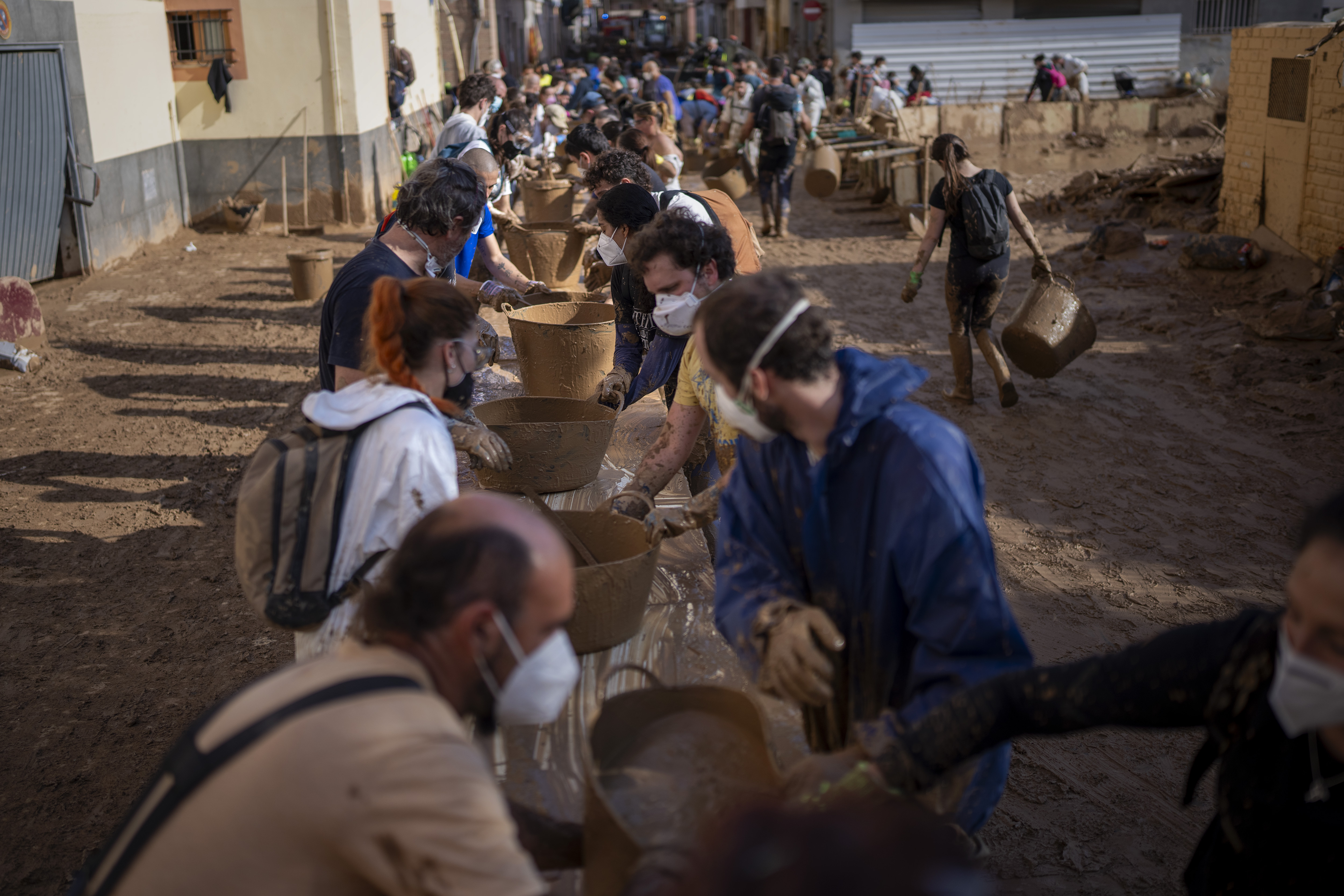 Volunteers make a human chain to evacuate the mud in buckets in an area still flooded with mud in Masanasa, Valencia, Spain, Thursday, Nov. 7, 2024. (AP Photo/Emilio Morenatti)