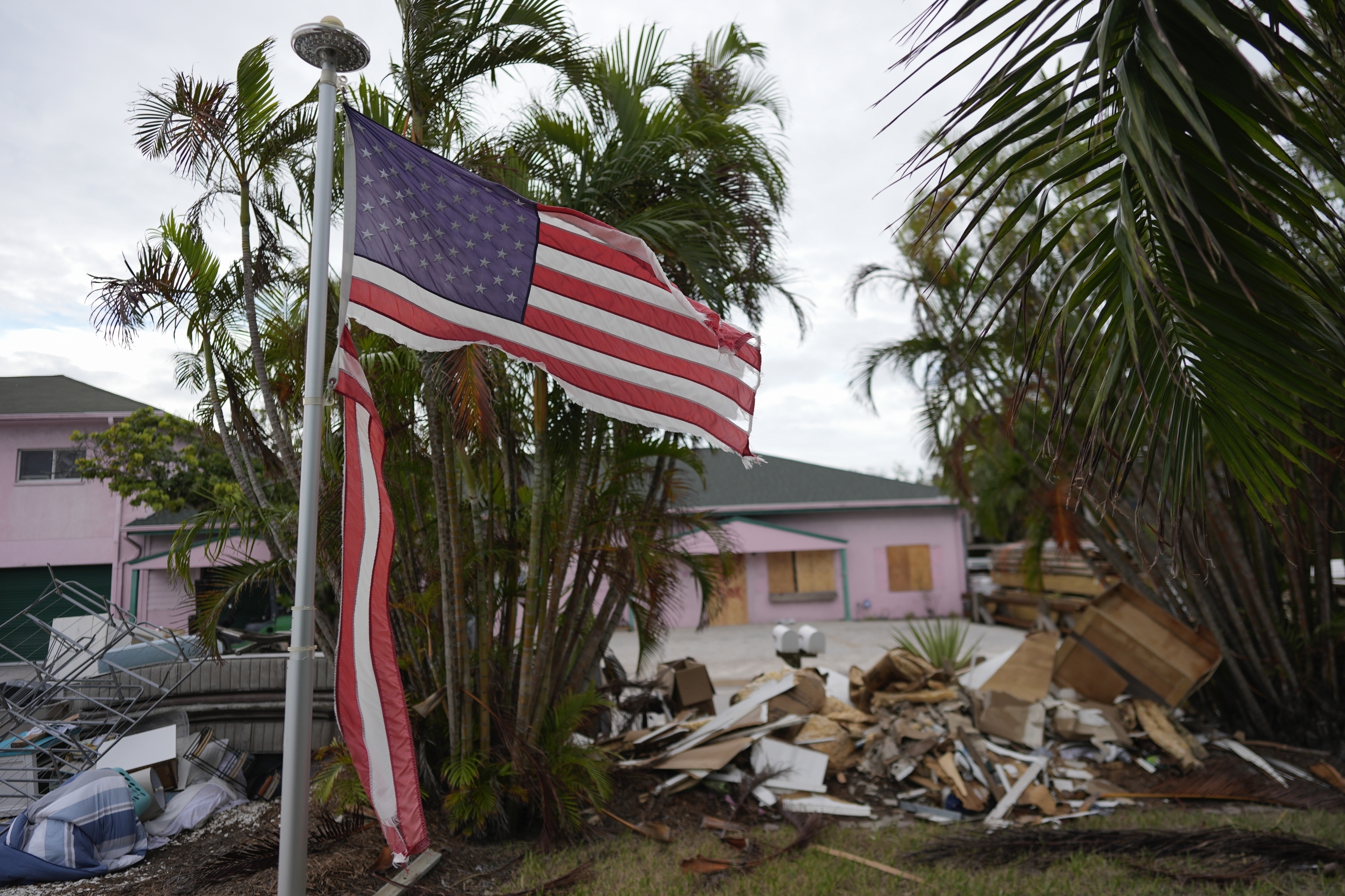 FILE - A tattered American flag flaps outside a home with furniture and household items damaged by Hurricane Helene piled outside along the street awaiting pickup ahead of the arrival of Hurricane Milton in Holmes Beach on Anna Maria Island, Fla., Oct. 8, 2024. (AP Photo/Rebecca Blackwell, File)