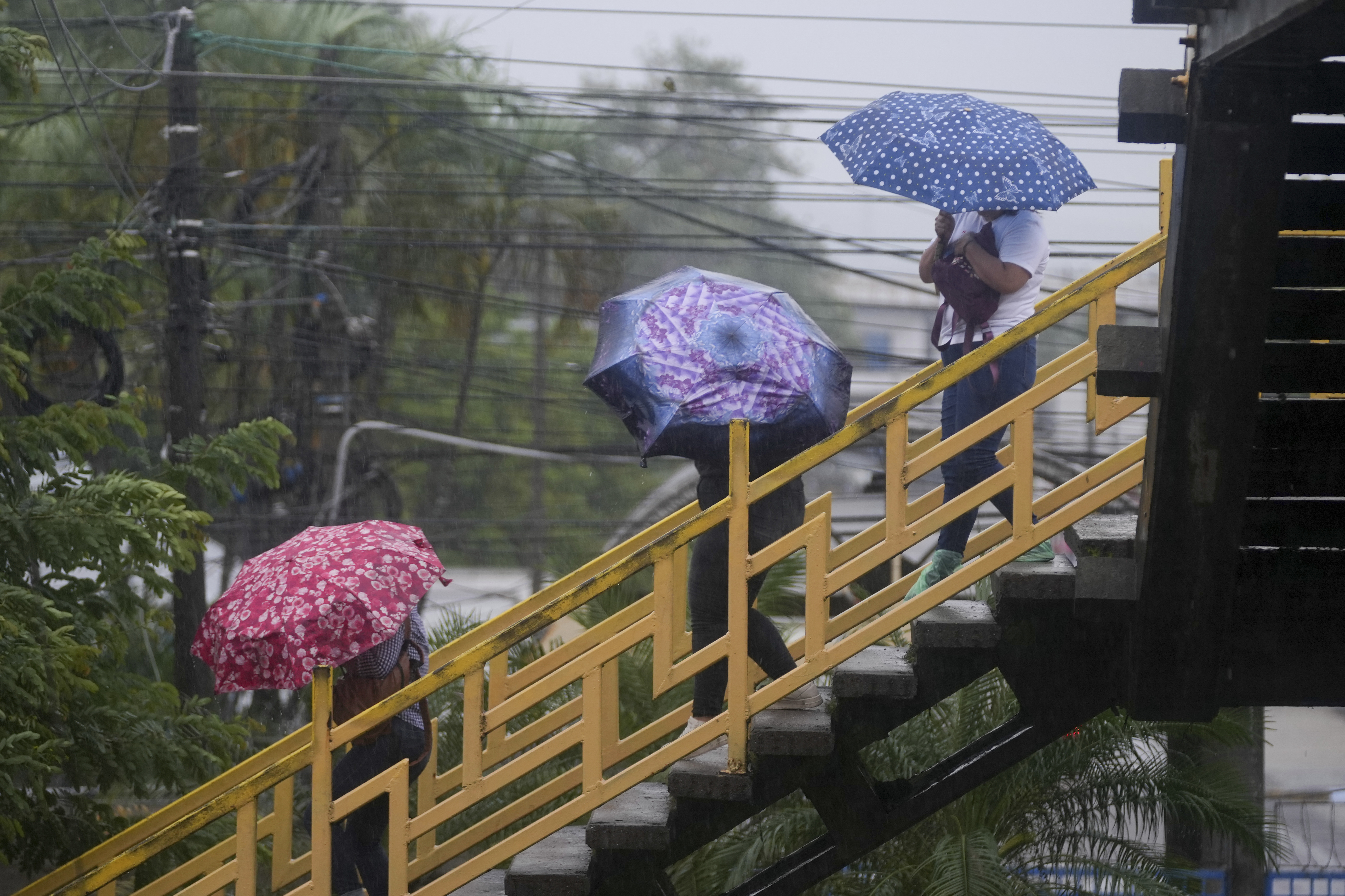 People cross a pedestrian bridge during rains brought on by tropical storm Sara in San Pedro Sula, Honduras, Friday, Nov. 15, 2024. (AP Photo/Moises Castillo)