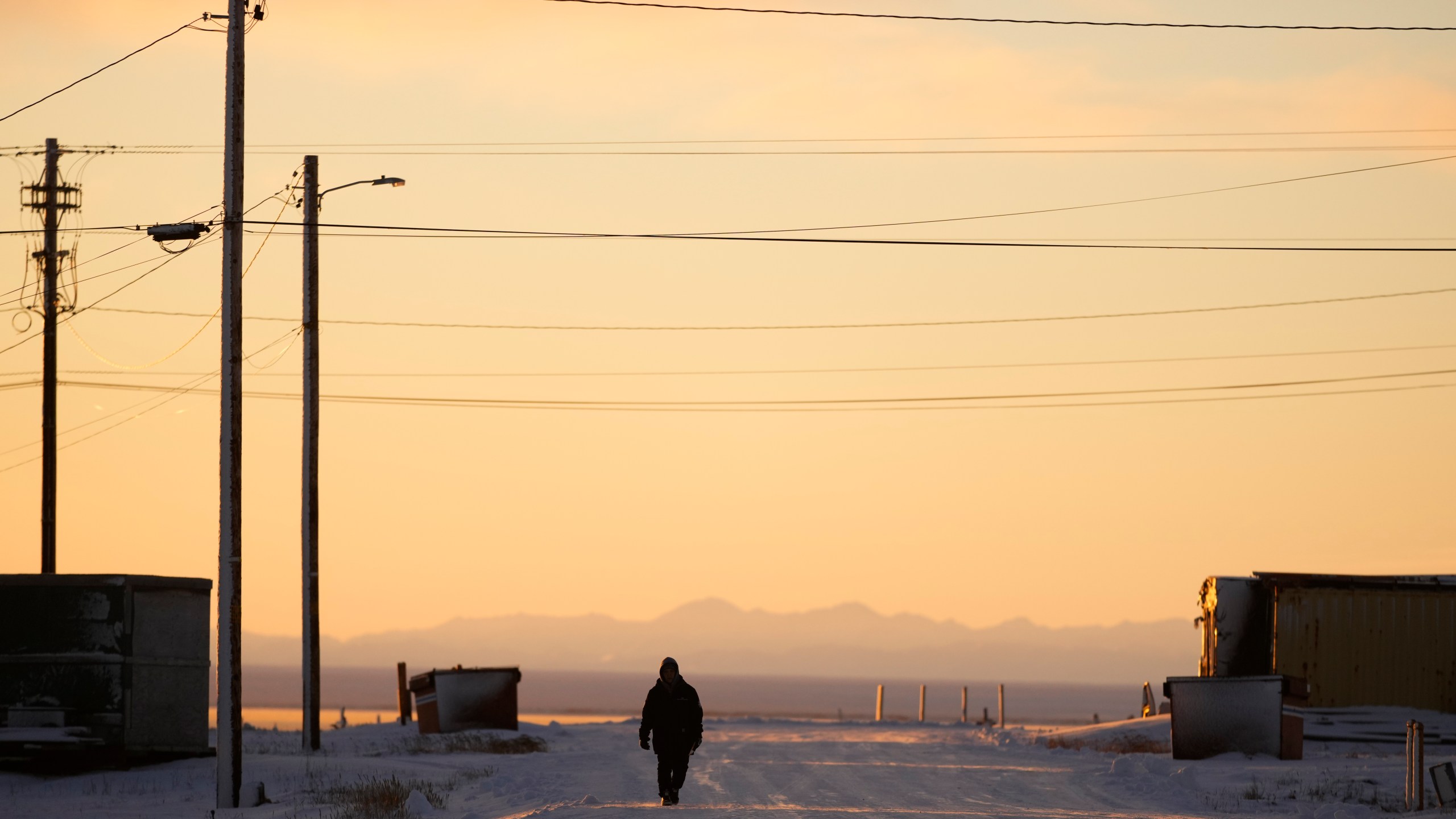 A resident walks up a street as the sun rises Tuesday, Oct. 15, 2024, in Kaktovik, Alaska. (AP Photo/Lindsey Wasson)