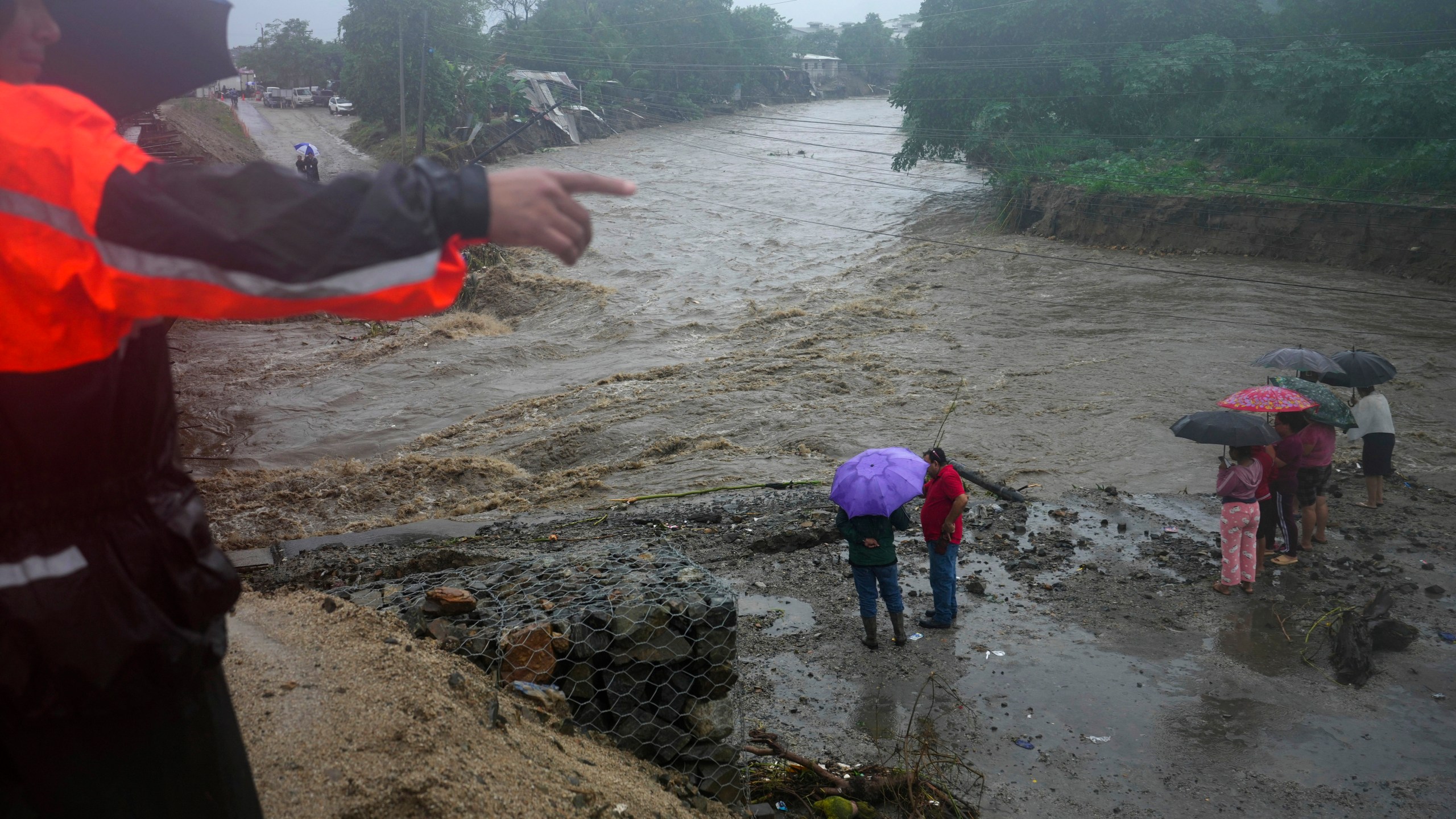 Residents stand alongside the banks of a river overrun by rains brought on by Tropical Storm Sara, on the outskirts of San Pedro Sula, Honduras, Saturday, Nov. 16, 2024. (AP Photo/Moises Castillo)