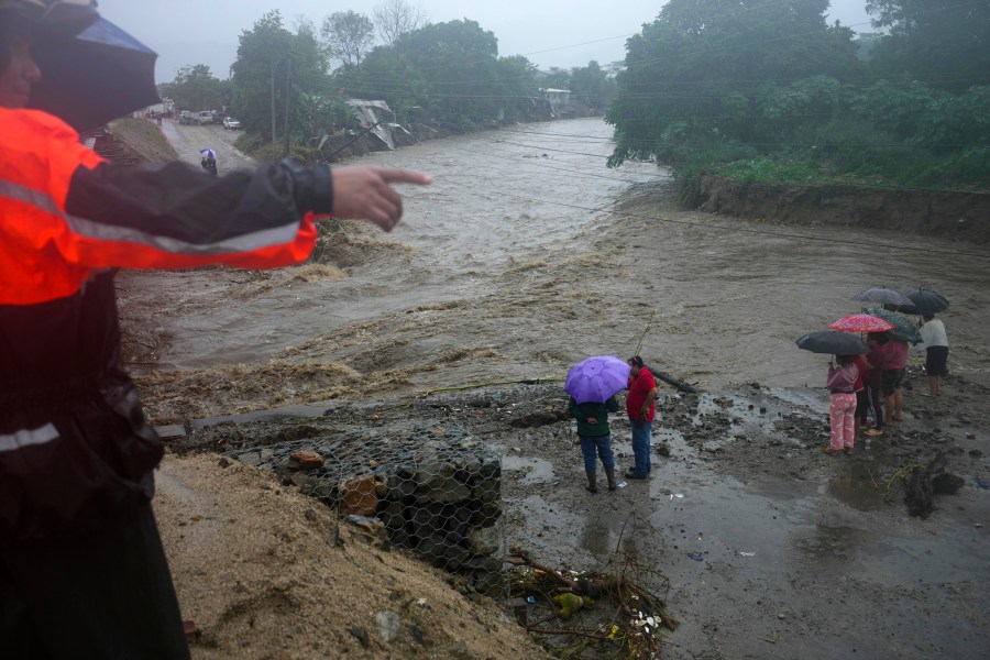 Residents stand alongside the banks of a river overrun by rains brought on by Tropical Storm Sara, on the outskirts of San Pedro Sula, Honduras, Saturday, Nov. 16, 2024. (AP Photo/Moises Castillo)