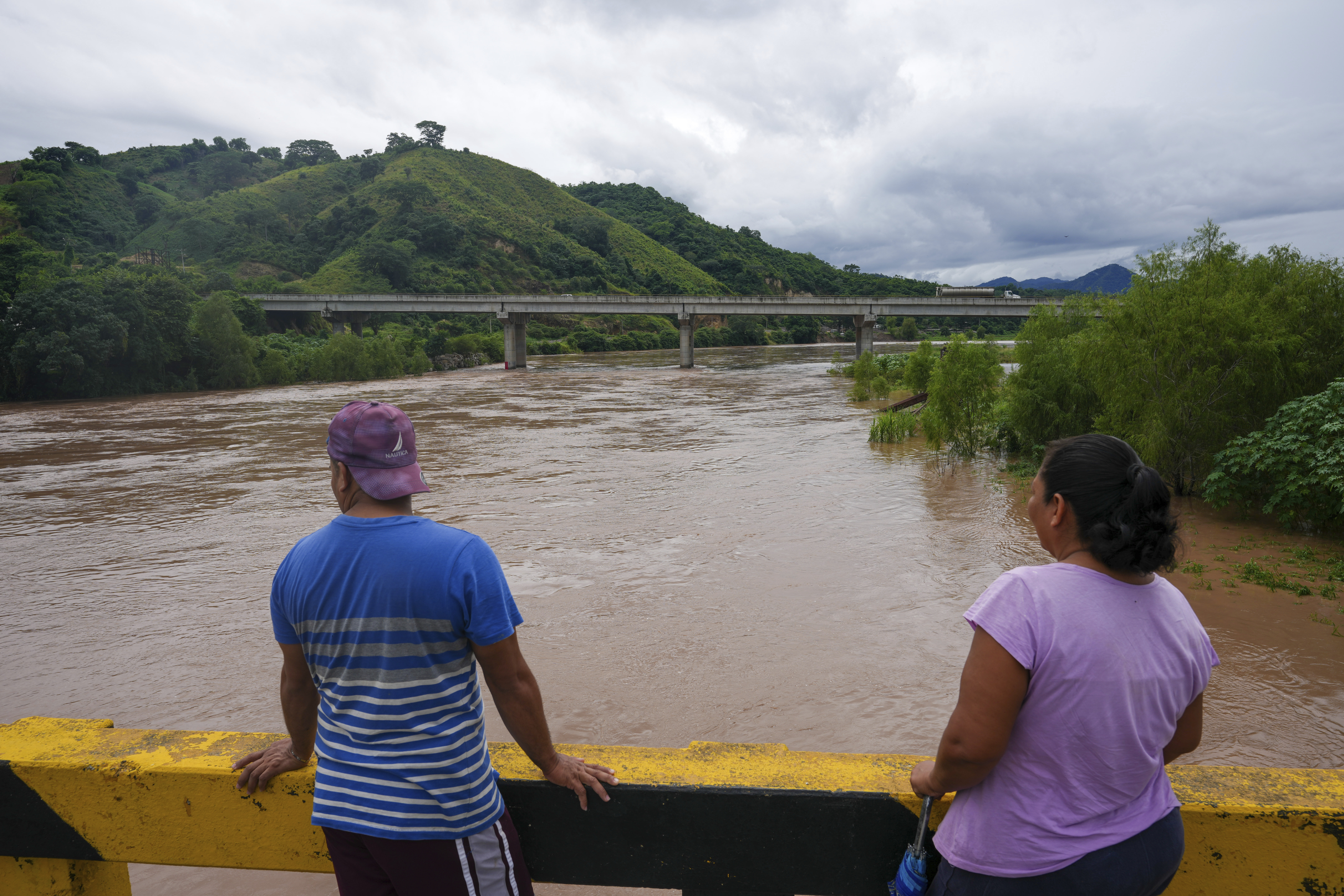 People standing on a bridge to watch the overflowing Ulúa River after Tropical Storm Sara, in Potrerillos, Honduras, Sunday, Nov. 17, 2024. (AP Photo/Moises Castillo)