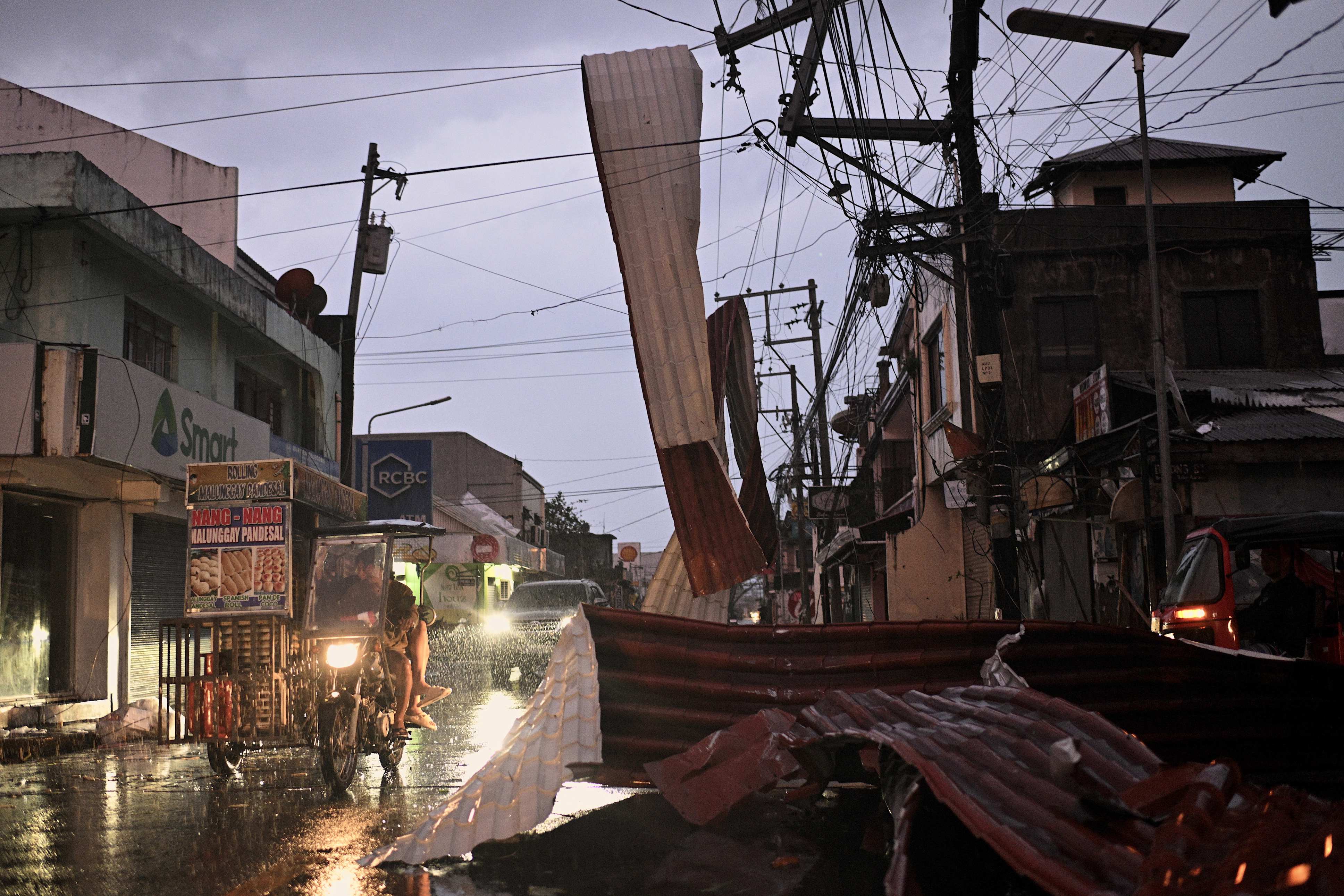 Motorists ride past a part of a roof suspended on electric wires blown by strong winds caused by Typhoon Man-yi along a street in the municipality of Baler, Aurora province, Philippines, Monday, Nov. 18, 2024. (AP Photo/Noel Celis)