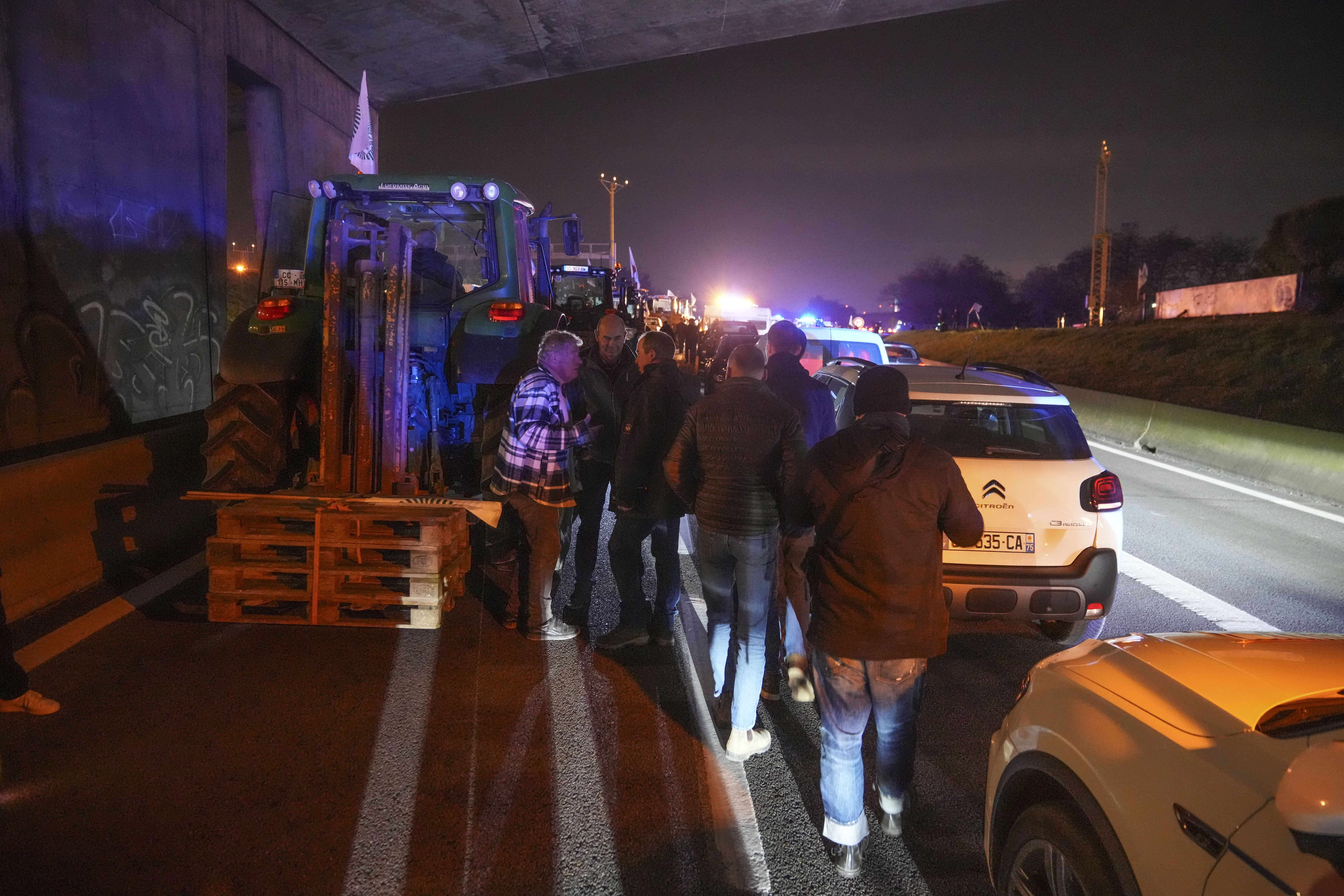 Farmers walk between tractors and cars on a blocked highway in Velizy-Villacoublay, outside Paris, Sunday, Nov. 17, 2024. (AP Photo/Michel Euler)