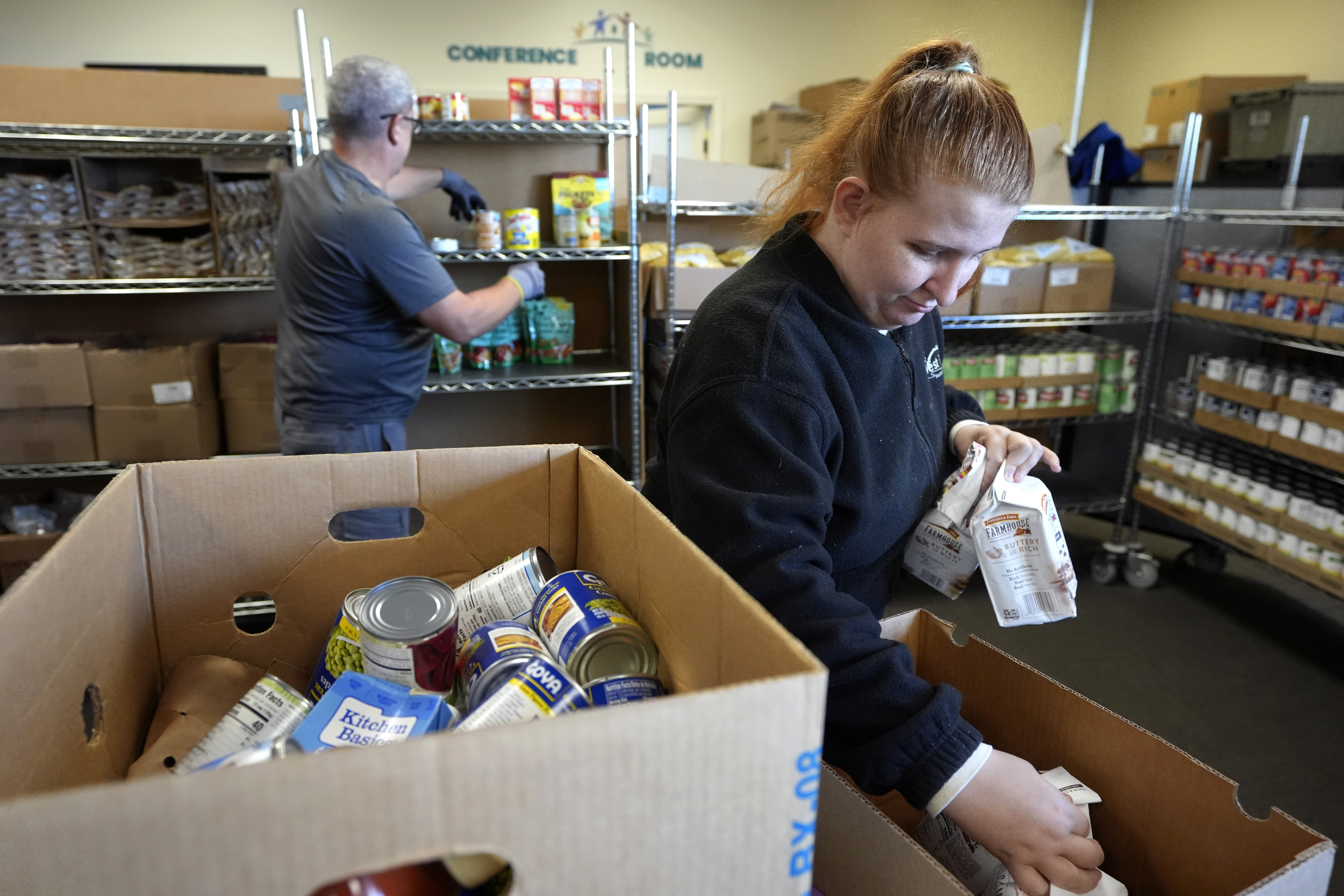 Volunteer Madison Turner, of Providence, R.I. right, organizes food items in a food pantry at Federal Hill House, Tuesday, Nov. 12, 2024, in Providence, R.I. (AP Photo/Steven Senne)