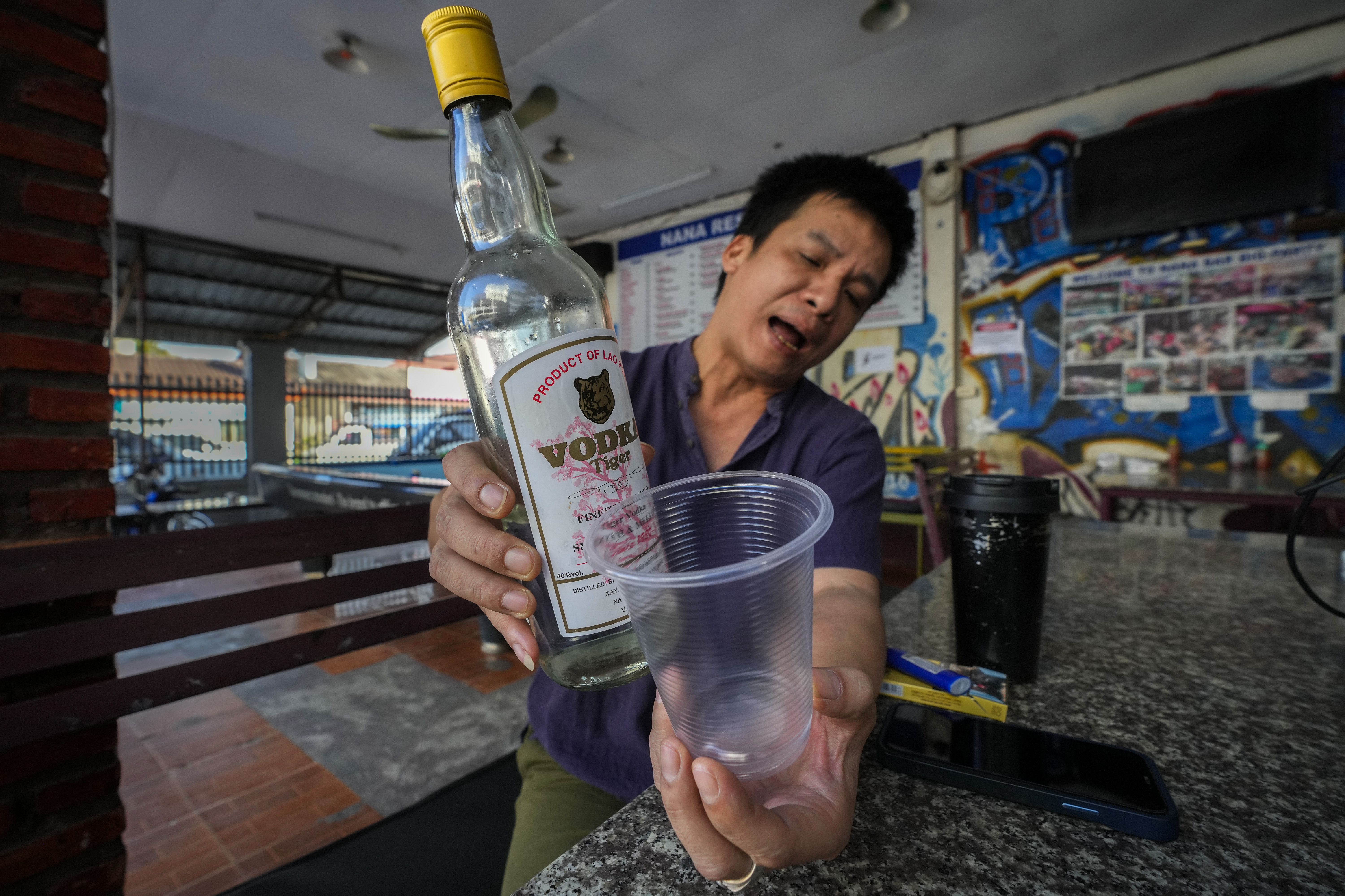 Duong Duc Toan, the manager of Nana Backpack hostel displays a bottle of vodka, in the bar of the hostel in Vang Vieng, Laos, Tuesday, Nov. 19, 2024. (AP Photo/Anupam Nath)