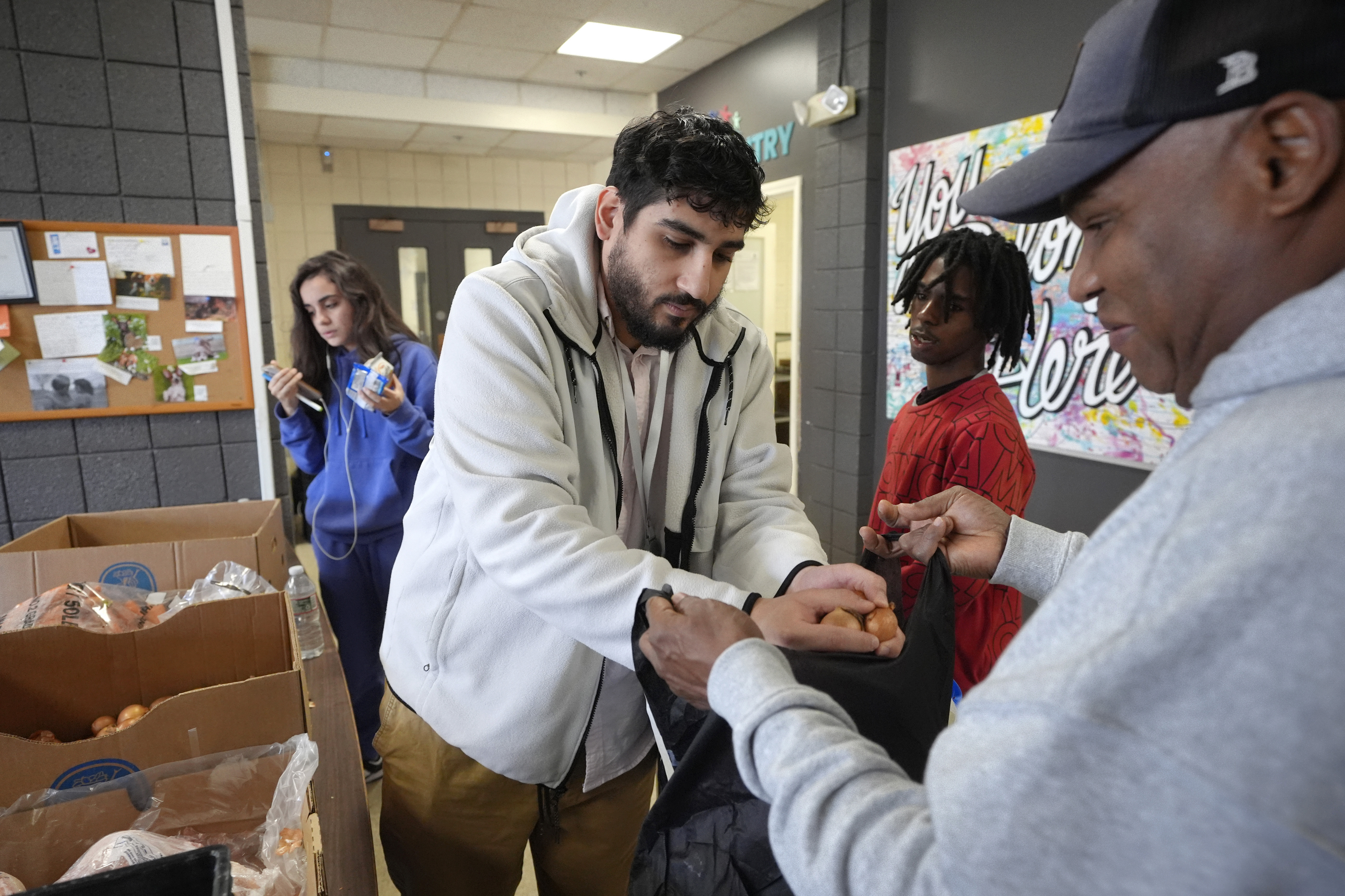 Volunteer Charles Mena, of Providence, R.I. center, places food in a bag for customer Hungria Hernandez Diomedes, right, in a food pantry at Federal Hill House, Tuesday, Nov. 12, 2024, in Providence, R.I. (AP Photo/Steven Senne)