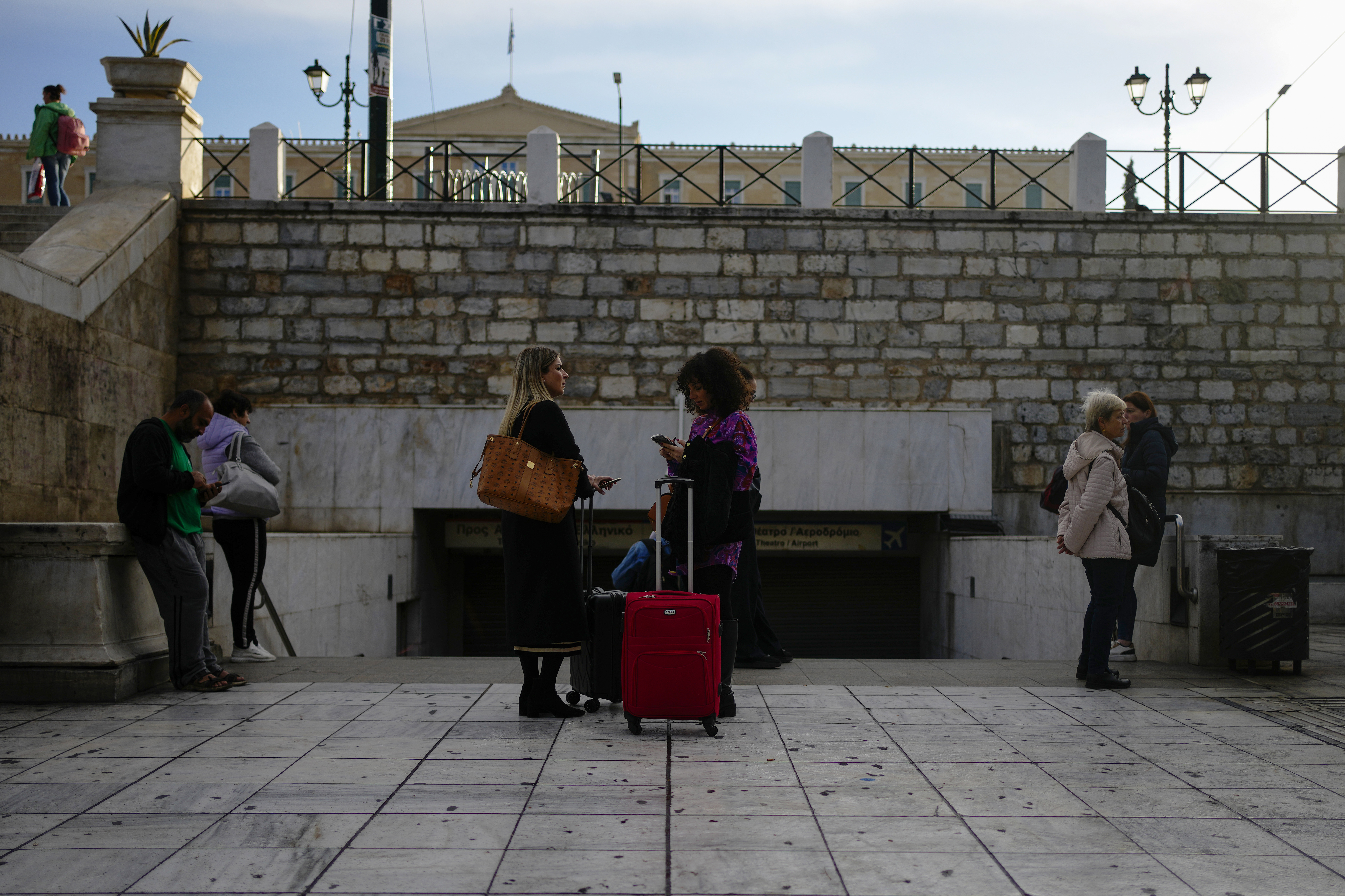 Commuters stand outside the closed main metro Syntagma station, during a nationwide general strike organized by private and public sector unions demanding for better wages, in Athens, Greece, Wednesday, Nov. 20, 2024. (AP Photo/Thanassis Stavrakis)