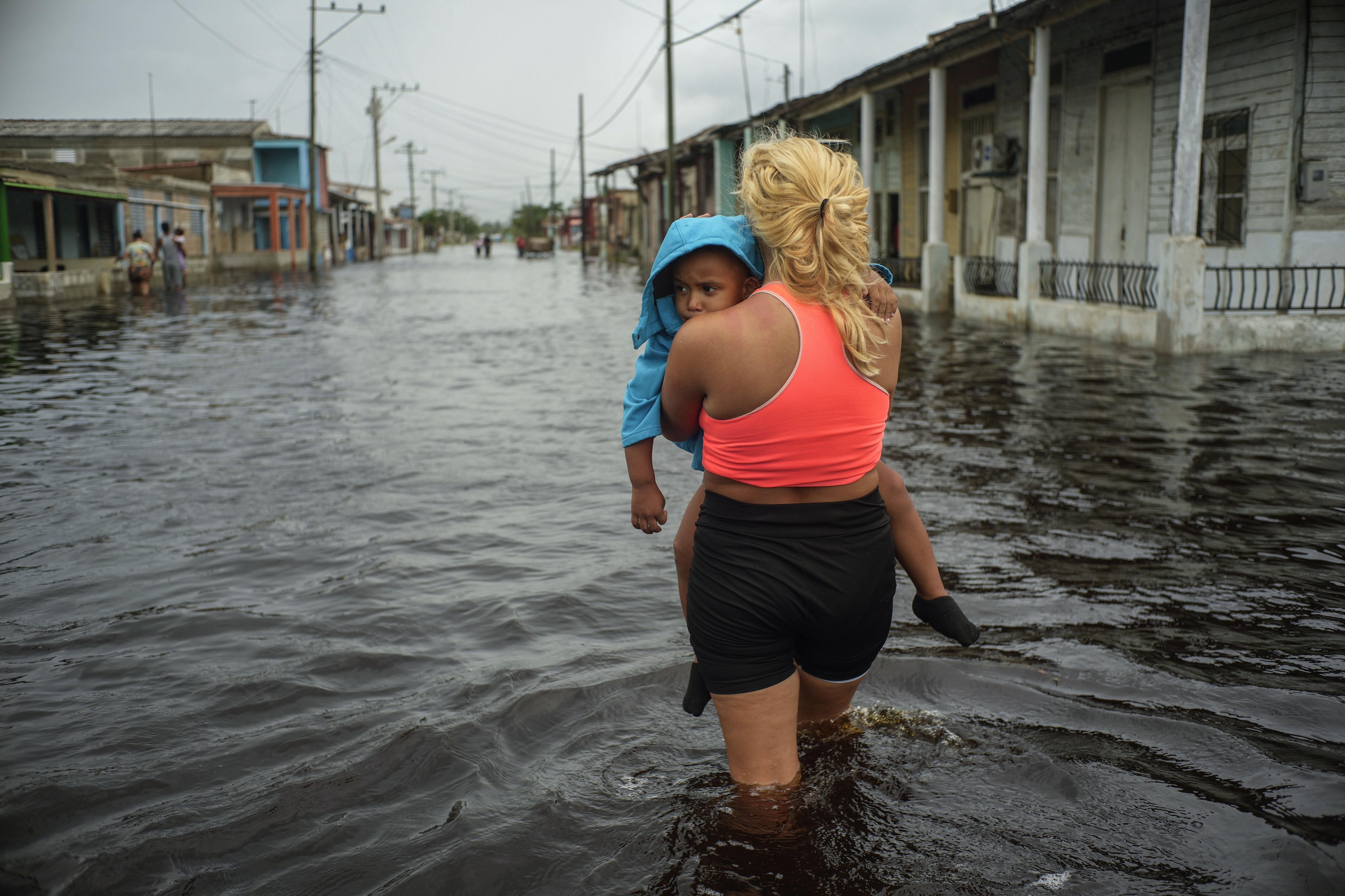 FILE - A woman carries a child as she wades through a street flooded in the passing of Hurricane Helene, in Batabano, Mayabeque province, Cuba, Sept. 26, 2024. (AP Photo/Ramon Espinosa, File)