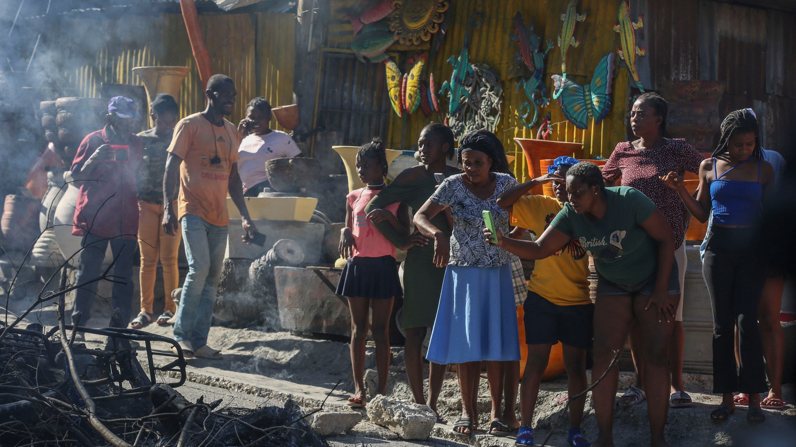 A woman films a scene where the bodies of suspected gang members who were set on fire by residents sit in a heap in the middle of a road, in the Pétion-Ville neighborhood of Port-au-Prince, Haiti, Tuesday, Nov. 19, 2024. (AP Photo/Odelyn Joseph)