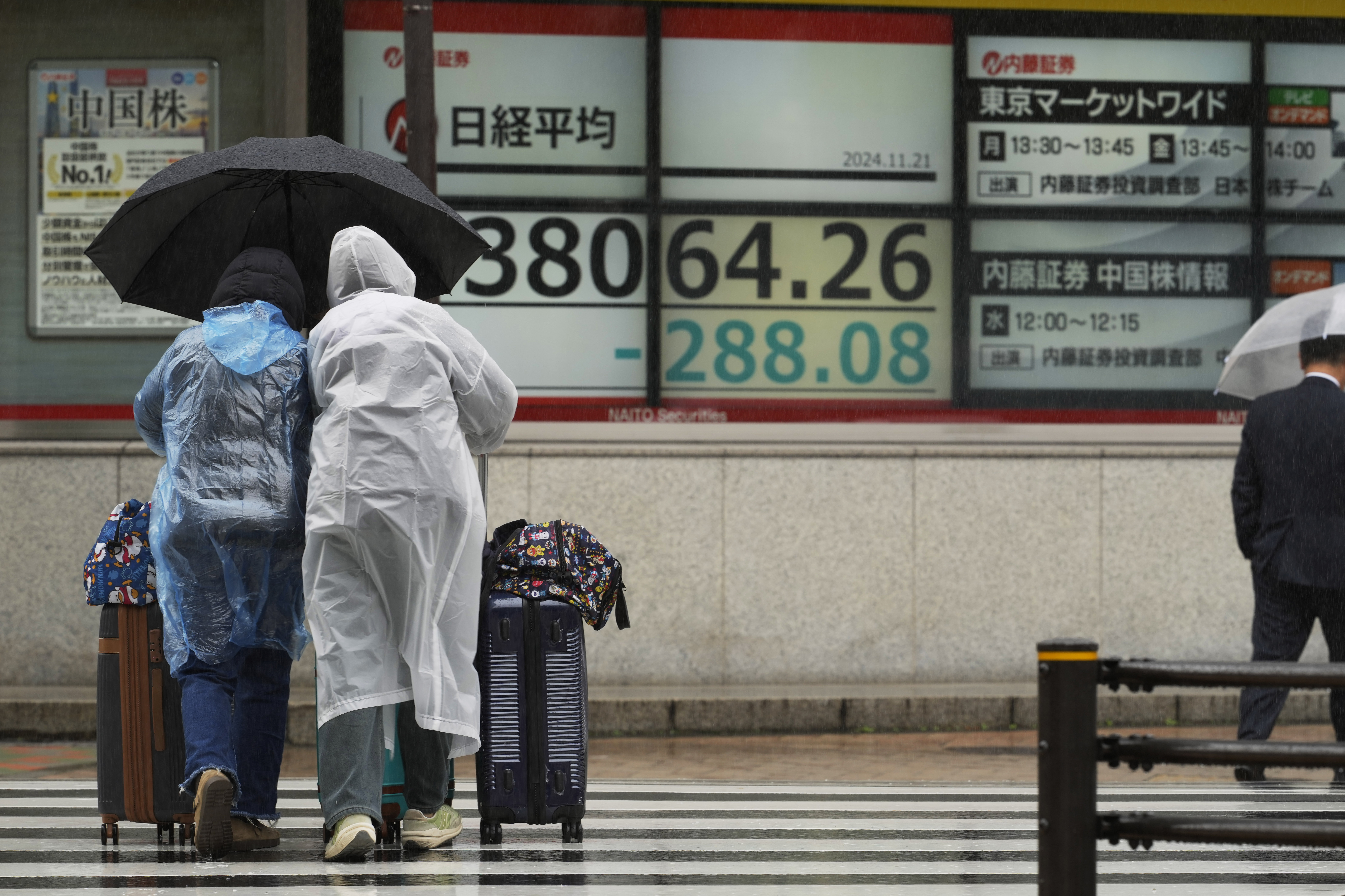 Travelers walk by monitors showing Japan's Nikkei 225 index at a securities firm in Tokyo, Thursday, Nov. 21, 2024. (AP Photo/Hiro Komae)