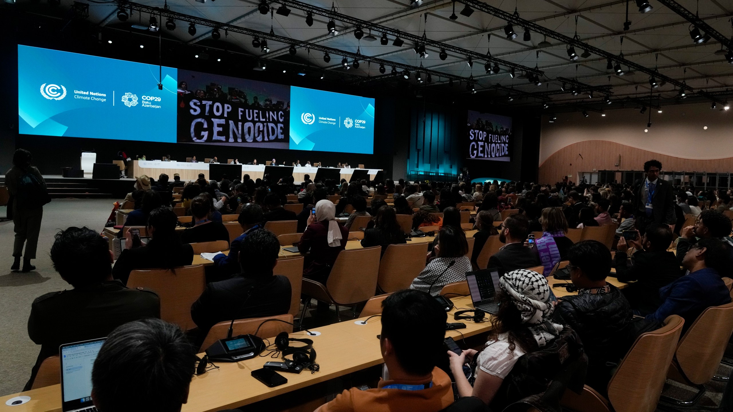 Activists display signs that read "stop fueling genocide" during the People's Plenary at the COP29 U.N. Climate Summit, Thursday, Nov. 21, 2024, in Baku, Azerbaijan. (AP Photo/Rafiq Maqbool)