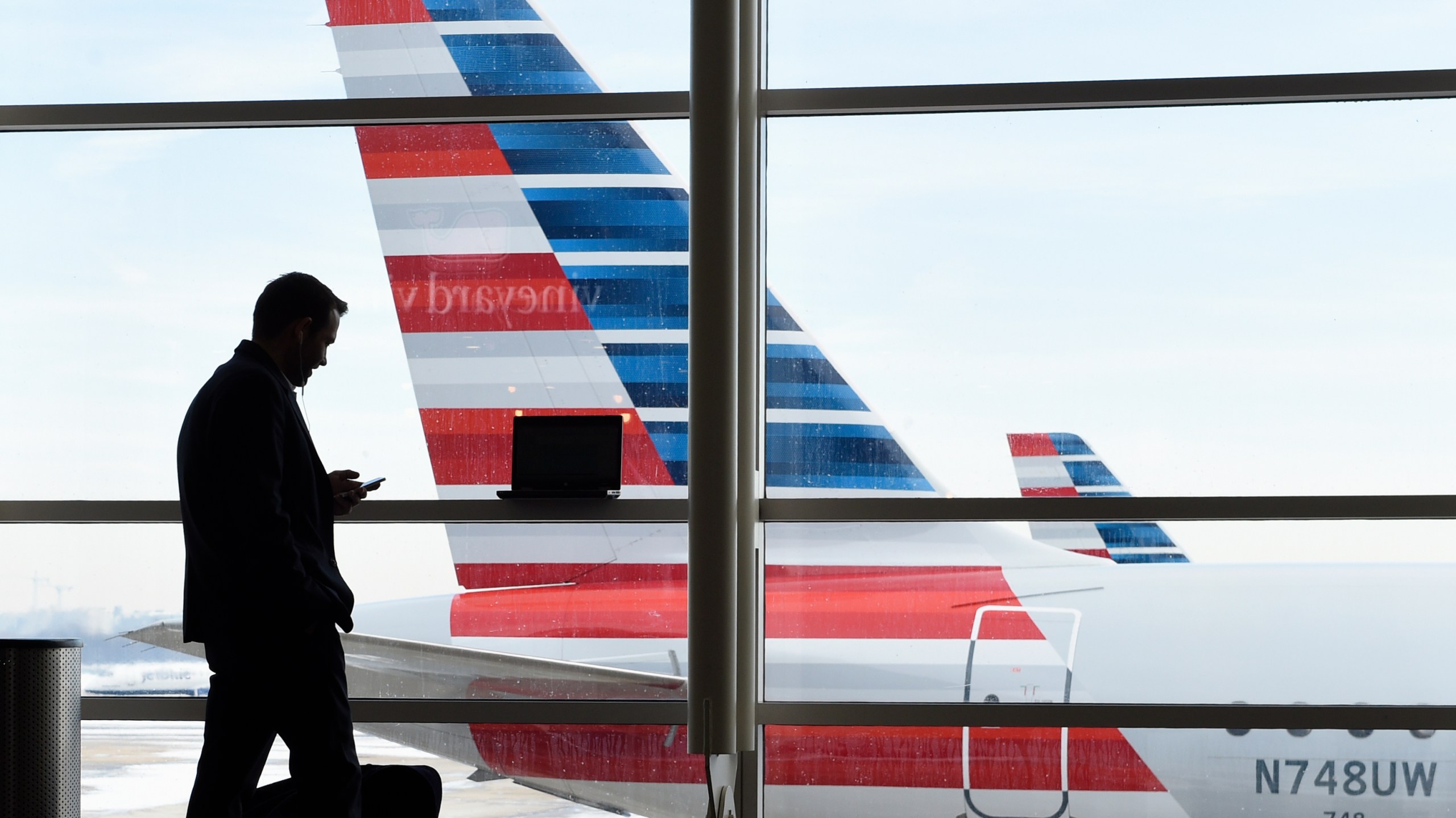 FILE - A passenger talks on the phone with American Airlines jets parked behind him at Washington's Ronald Reagan National Airport in Washington, Jan. 25, 2016. (AP Photo/Susan Walsh, File)