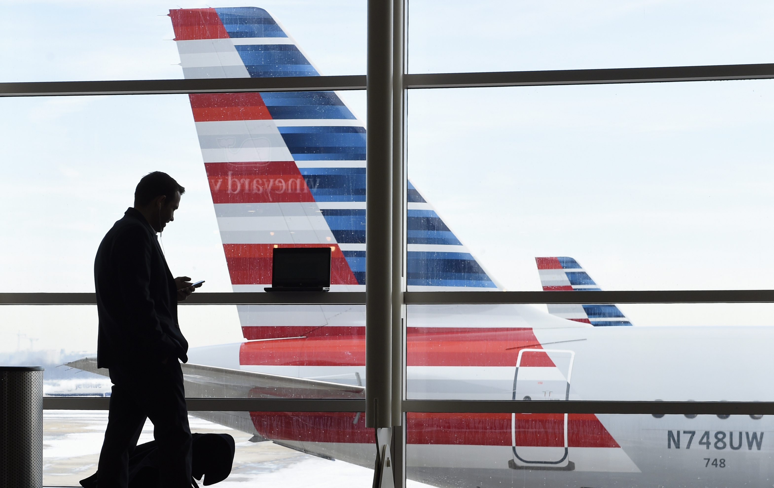 FILE - A passenger talks on the phone with American Airlines jets parked behind him at Washington's Ronald Reagan National Airport in Washington, Jan. 25, 2016. (AP Photo/Susan Walsh, File)