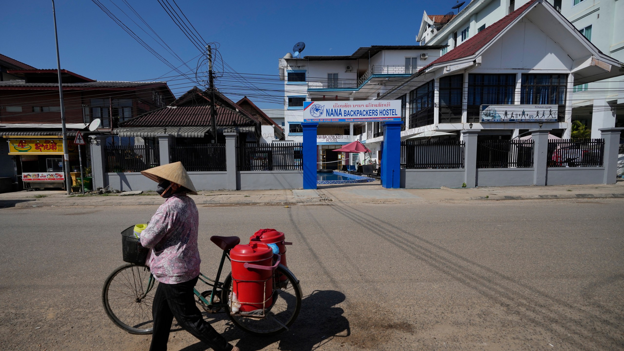 A woman with a bicycle walks pasts Nana Backpackers hostel in Vang Vieng, Laos, Friday, Nov. 22, 2024. (AP Photo/Anupam Nath)