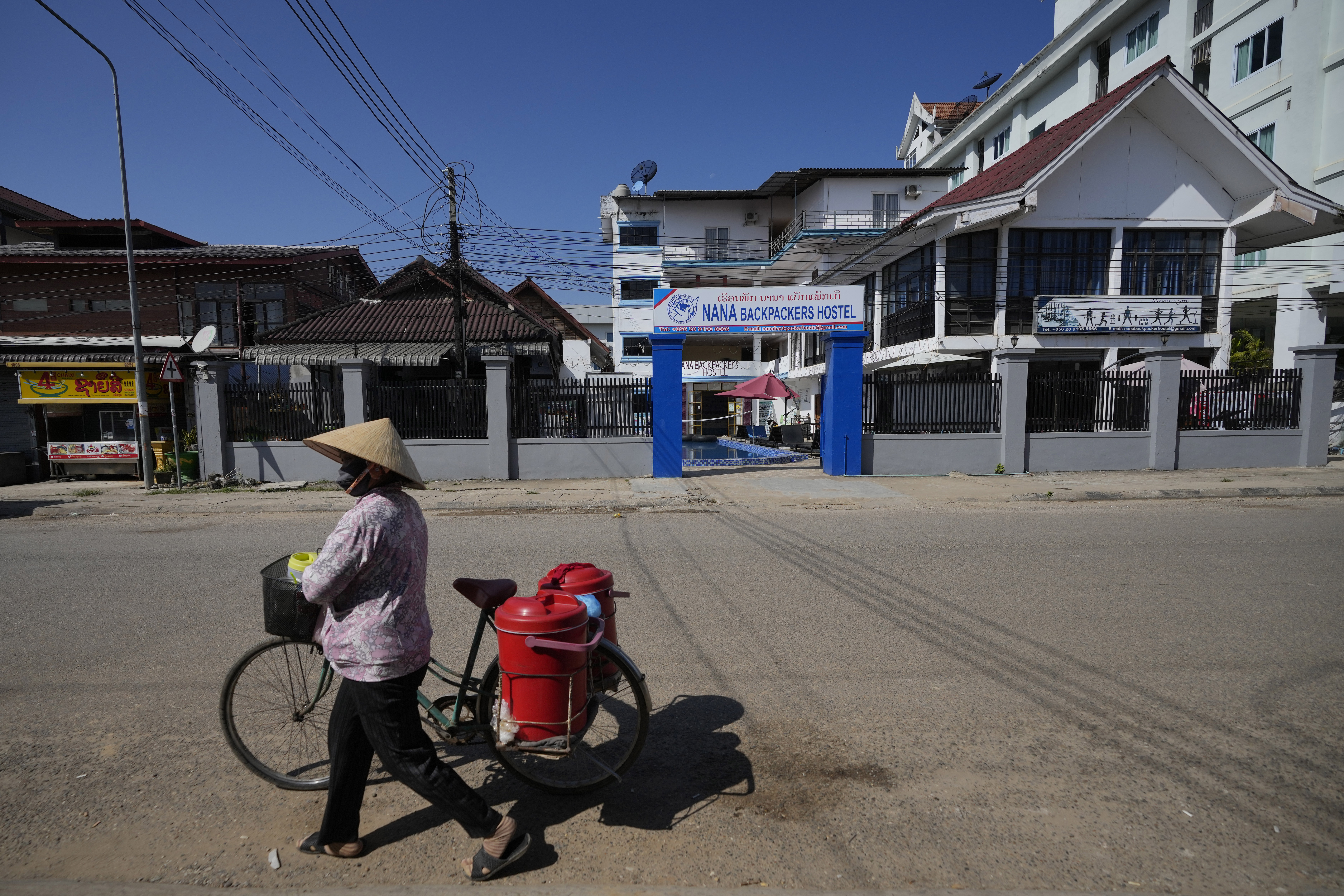 A woman with a bicycle walks pasts Nana Backpackers hostel in Vang Vieng, Laos, Friday, Nov. 22, 2024. (AP Photo/Anupam Nath)