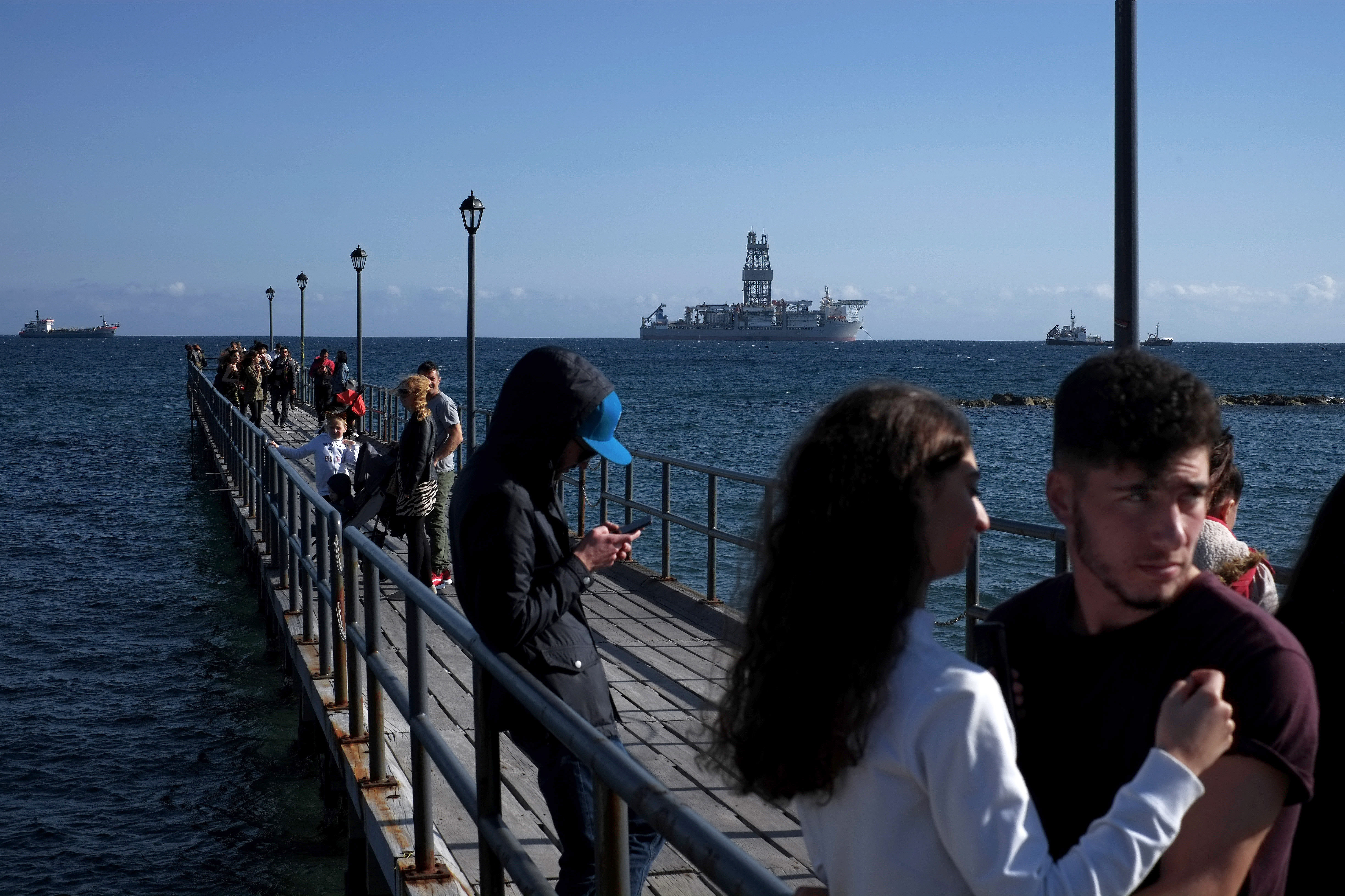 FILE - People walk at a dock with a drilling platform in the background, in the southern coastal city of Limassol, Cyprus, on March 10, 2019. (AP Photo/Petros Karadjias, File)