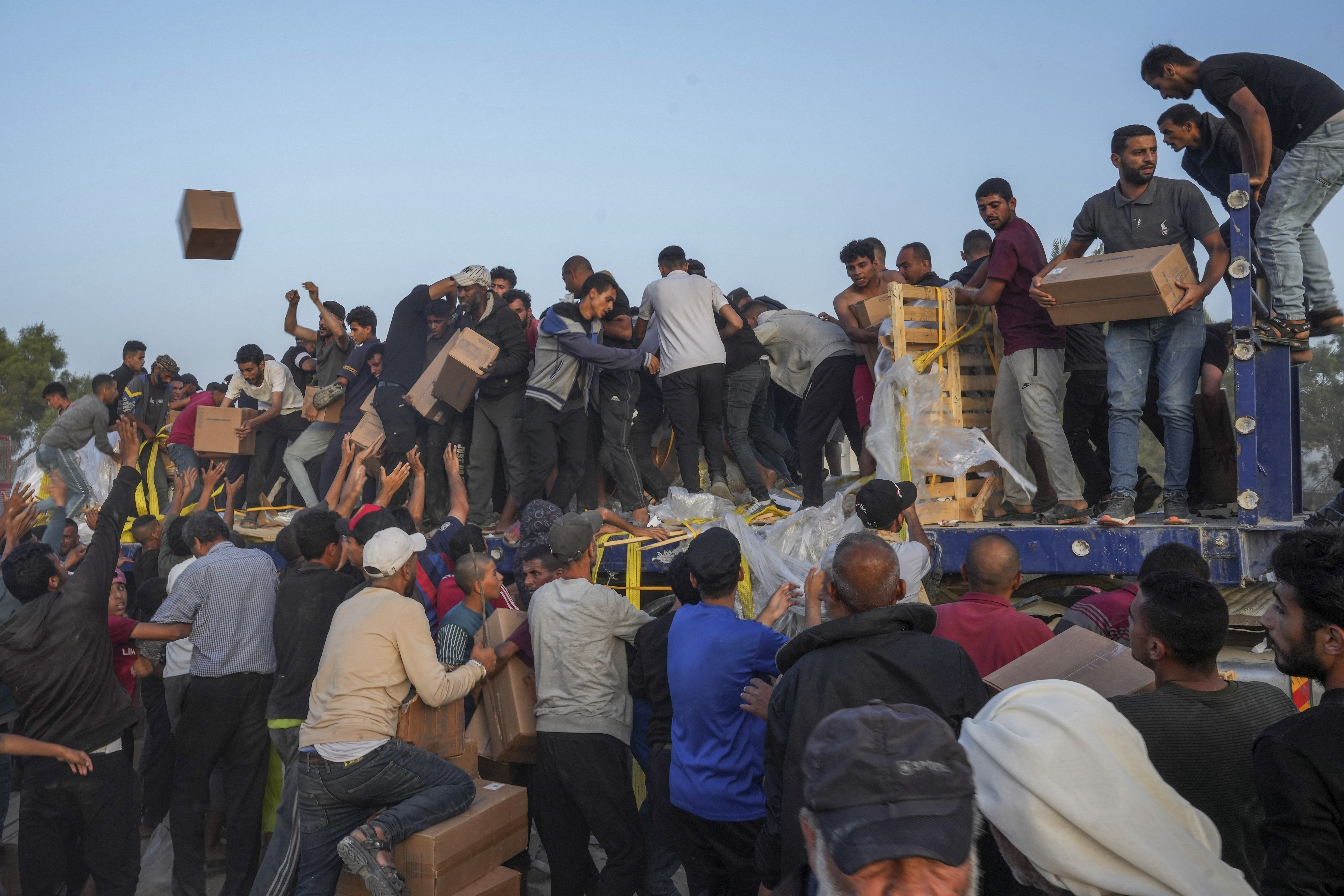 FILE - Palestinians storm trucks loaded with humanitarian aid brought in through a new U.S.-built pier, in the central Gaza Strip, on May 18, 2024. (AP Photo/Abdel Kareem Hana, File)