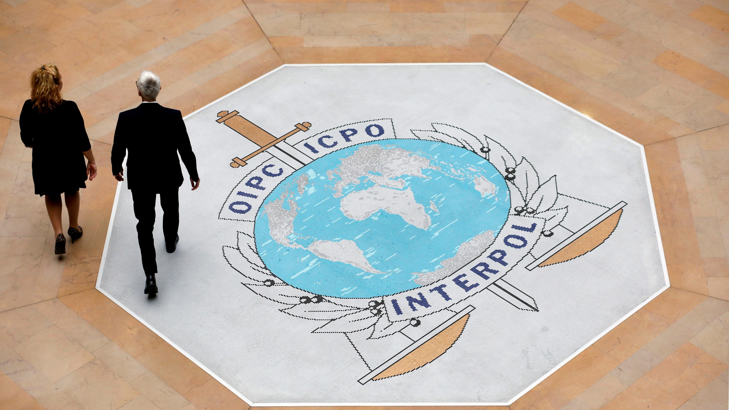 FILE - People walk on the Interpol logo at the international police agency headquarters in Lyon, France, on Nov. 8, 2018. (AP Photo/Laurent Cipriani, File)