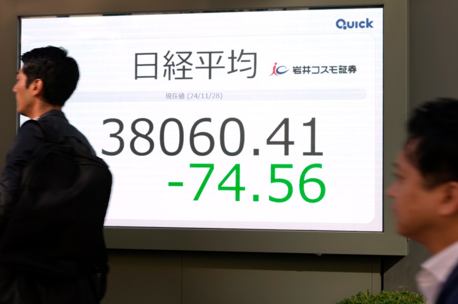 People walk past an electronic stock board showing Japan's Nikkei 225 stock index at a securities firm, Thursday, Nov. 28, 2024 in Tokyo. (AP Photo/Shuji Kajiyama)