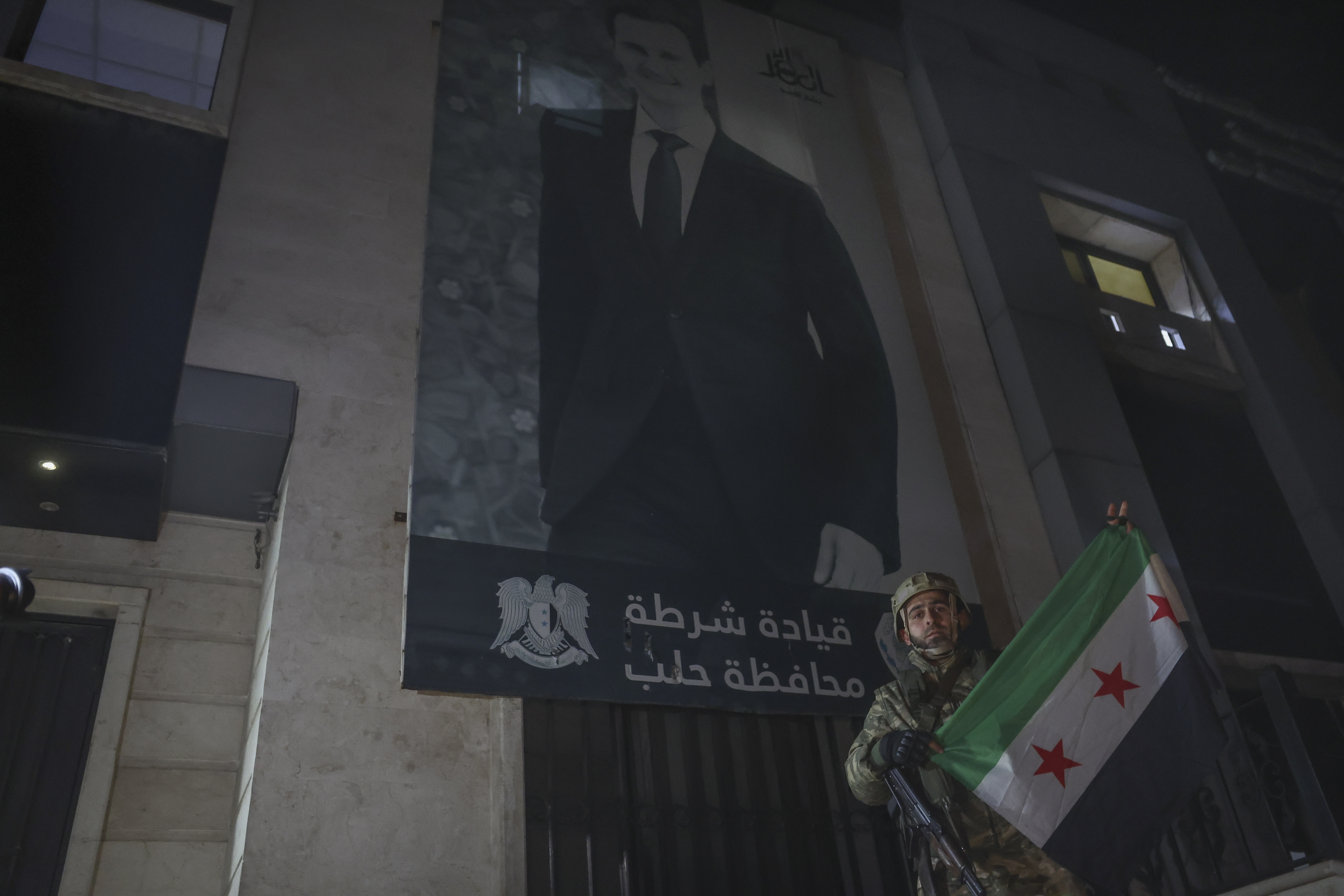 An opposition fighter poses with an opposition flag in front of a police station in Aleppo, Syria, late Friday, Nov. 29, 2024. (AP Photo/Ghaith Alsayed)