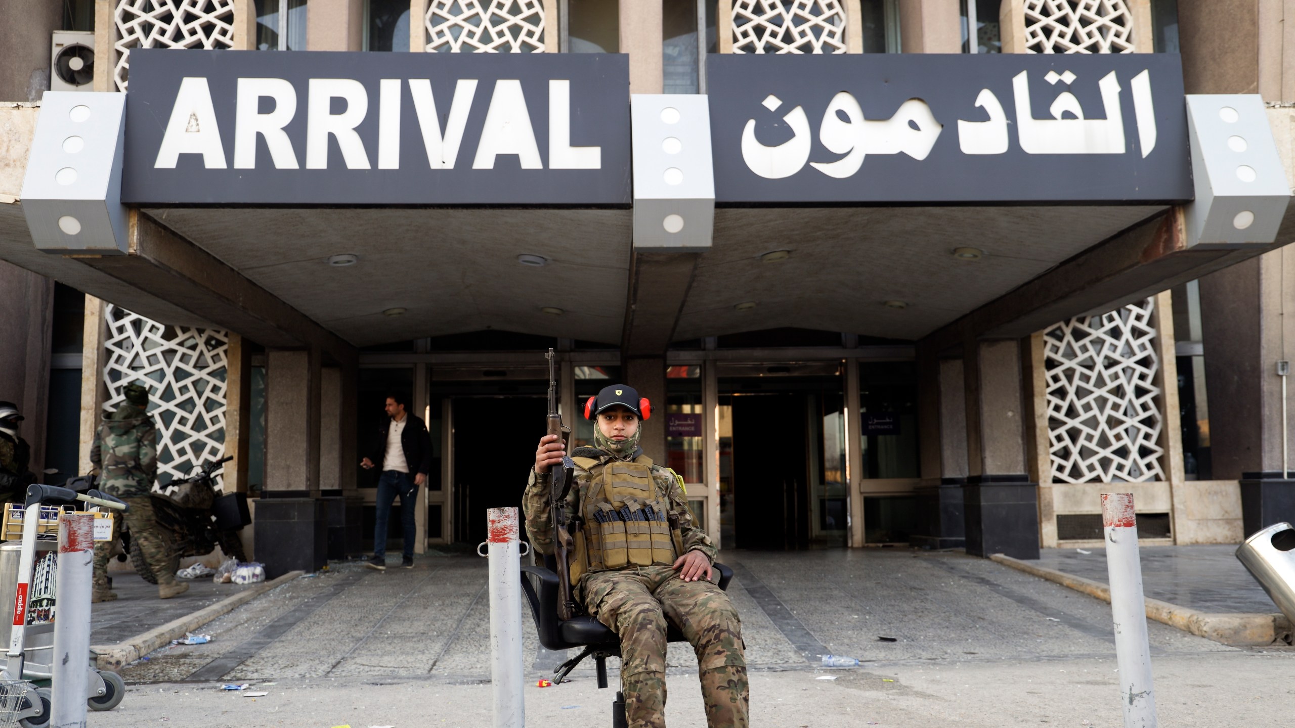 A Syrian opposition fighter sits on an office chair posing for a picture at arrivals gate of the Aleppo international airport in Aleppo, Syria, Monday, Dec. 2, 2024. .(AP Photo/Omar Albam)