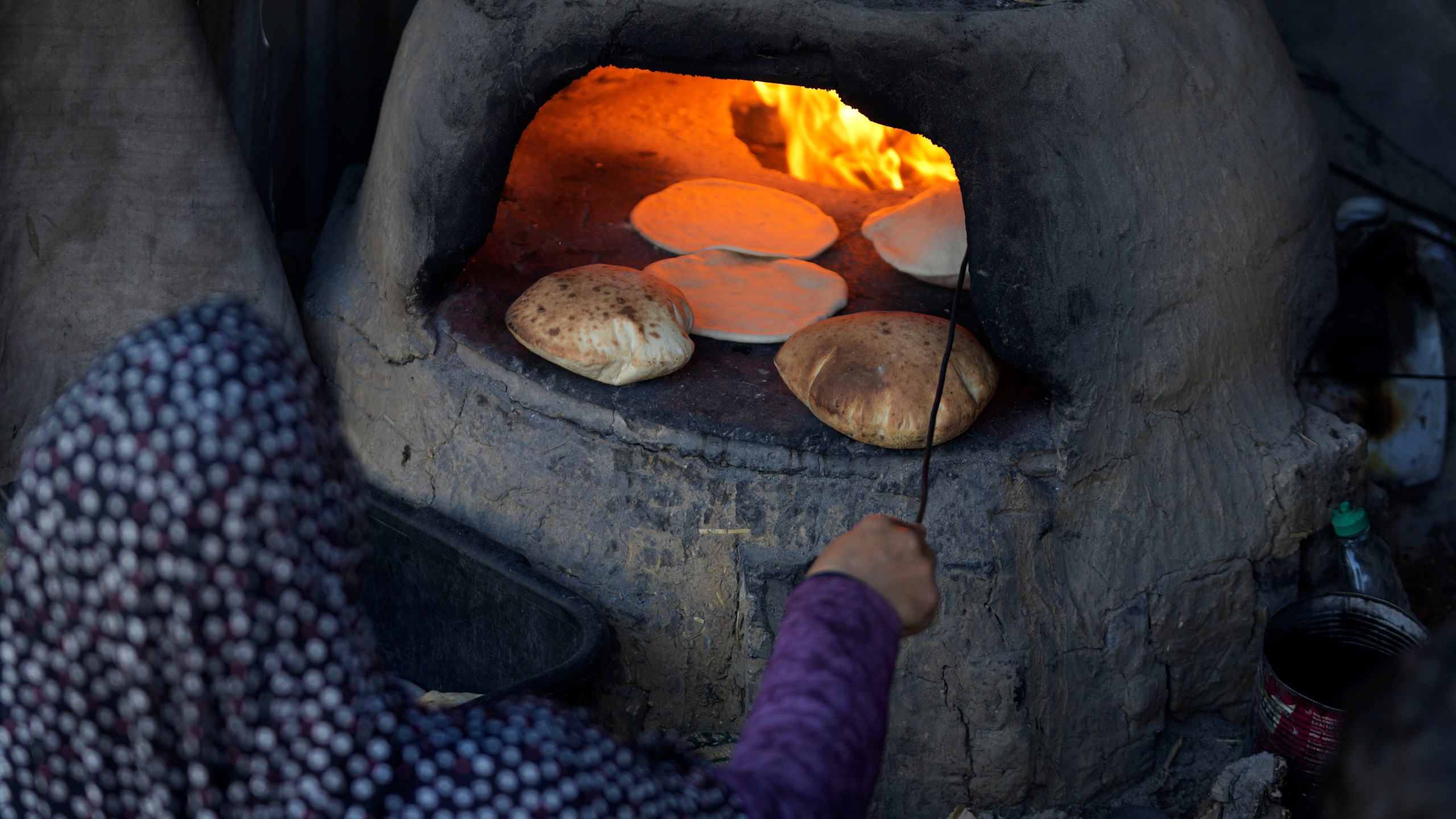 A Palestinian woman bakes bread in a clay oven amid dire food shortages in Deir al-Balah, Gaza Strip, Monday, Dec. 2, 2024. (AP Photo/Abdel Kareem Hana)