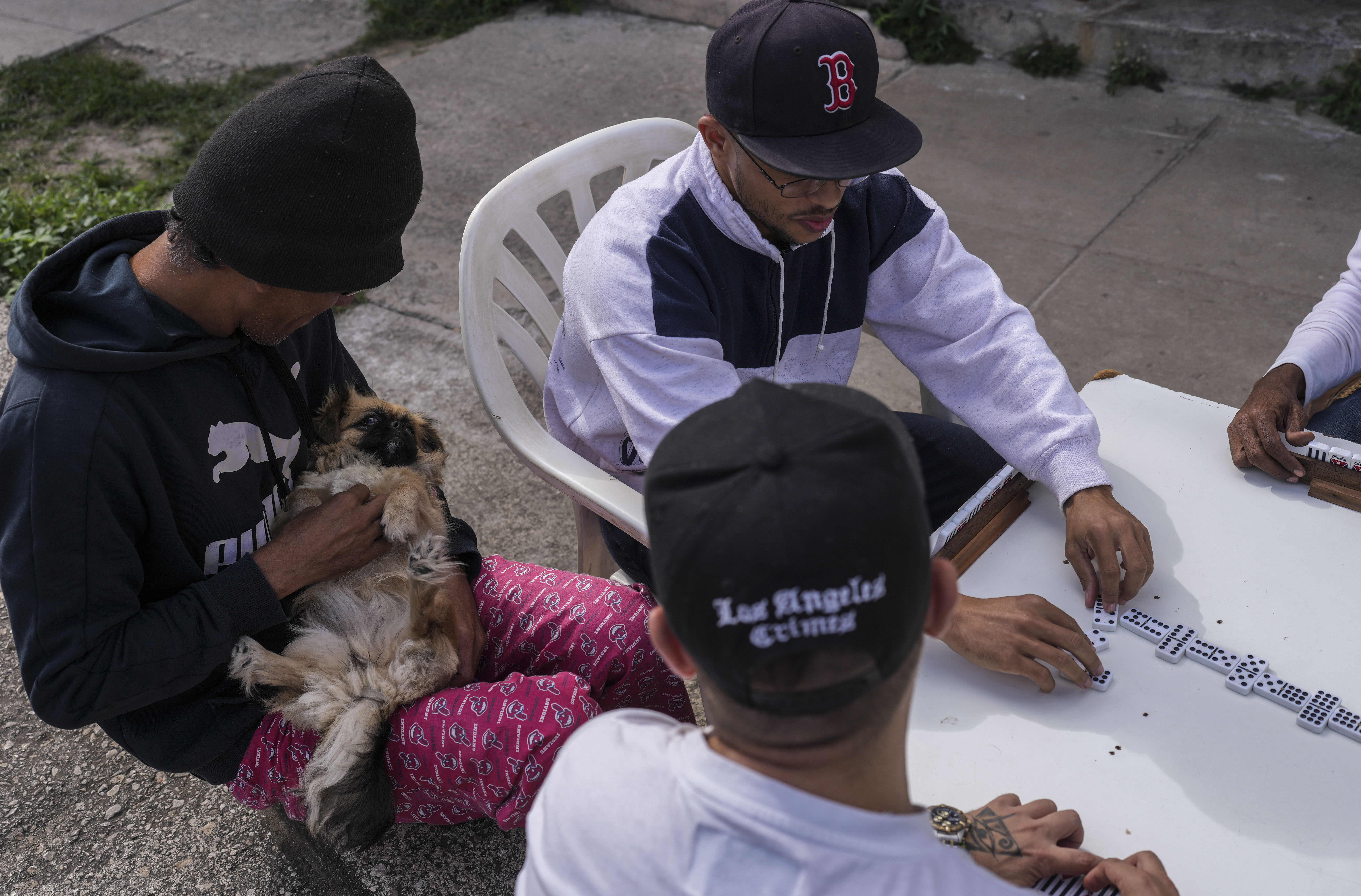 A man pets his dog as friends play dominoes outdoors during a blackout in Havana, Cuba, Wednesday, Dec. 4, 2024. (AP Photo/Ramon Espinosa)