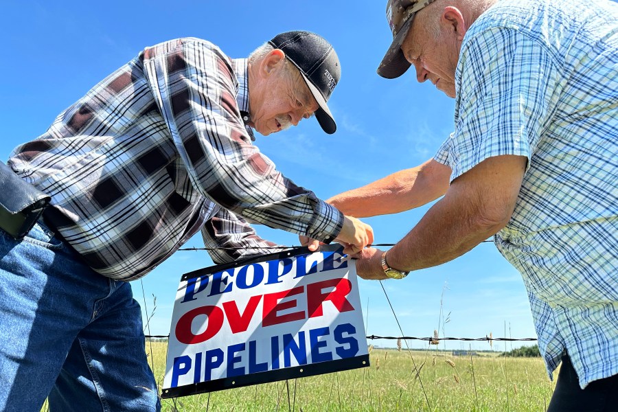 FILE - Gaylen Dewing, left, and Marvin Abraham affix a sign to a roadside fence east of Bismarck, N.D., Tuesday, Aug. 15, 2023, in opposition to Summit Carbon Solutions' proposed five-state, 2,000-mile pipeline network to carry carbon dioxide emissions from dozens of Midwestern ethanol plants to North Dakota for permanent storage deep underground. (AP Photo/Jack Dura, File)