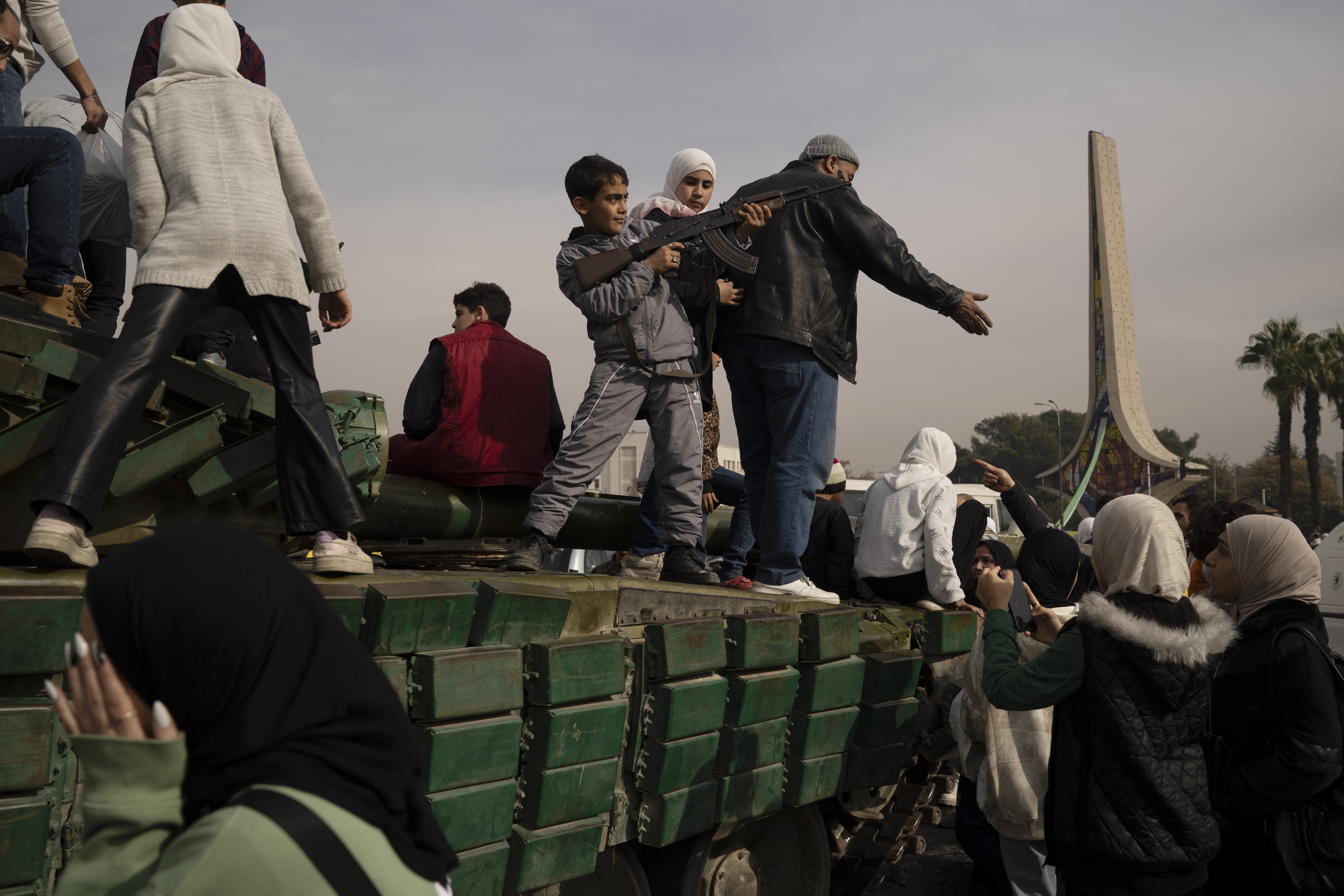 A boy holding a rifle borrowed from a Syrian opposition fighter poses on the top of a government forces tank that was left on a street, at the Umayyad Square in Damascus, Syria, Wednesday, Dec. 11, 2024. (AP Photo/Leo Correa)