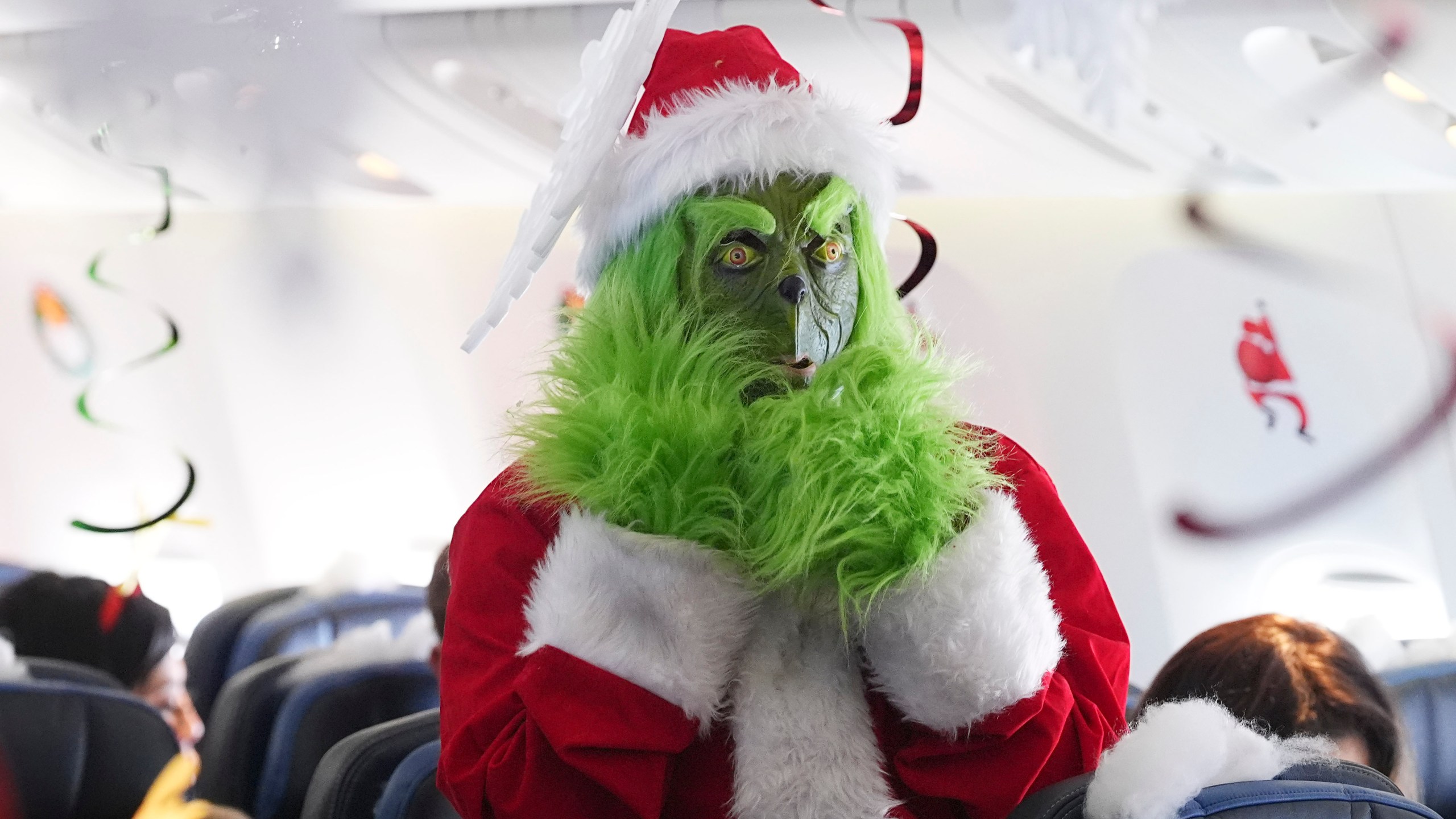 Dressed in a Grinch costume, a flight attendant entertains passengers during the United Airlines annual "fantasy flight" to a fictional North Pole at Denver International Airport, Saturday, Dec. 14, 2024, in Denver. (AP Photo/David Zalubowski)