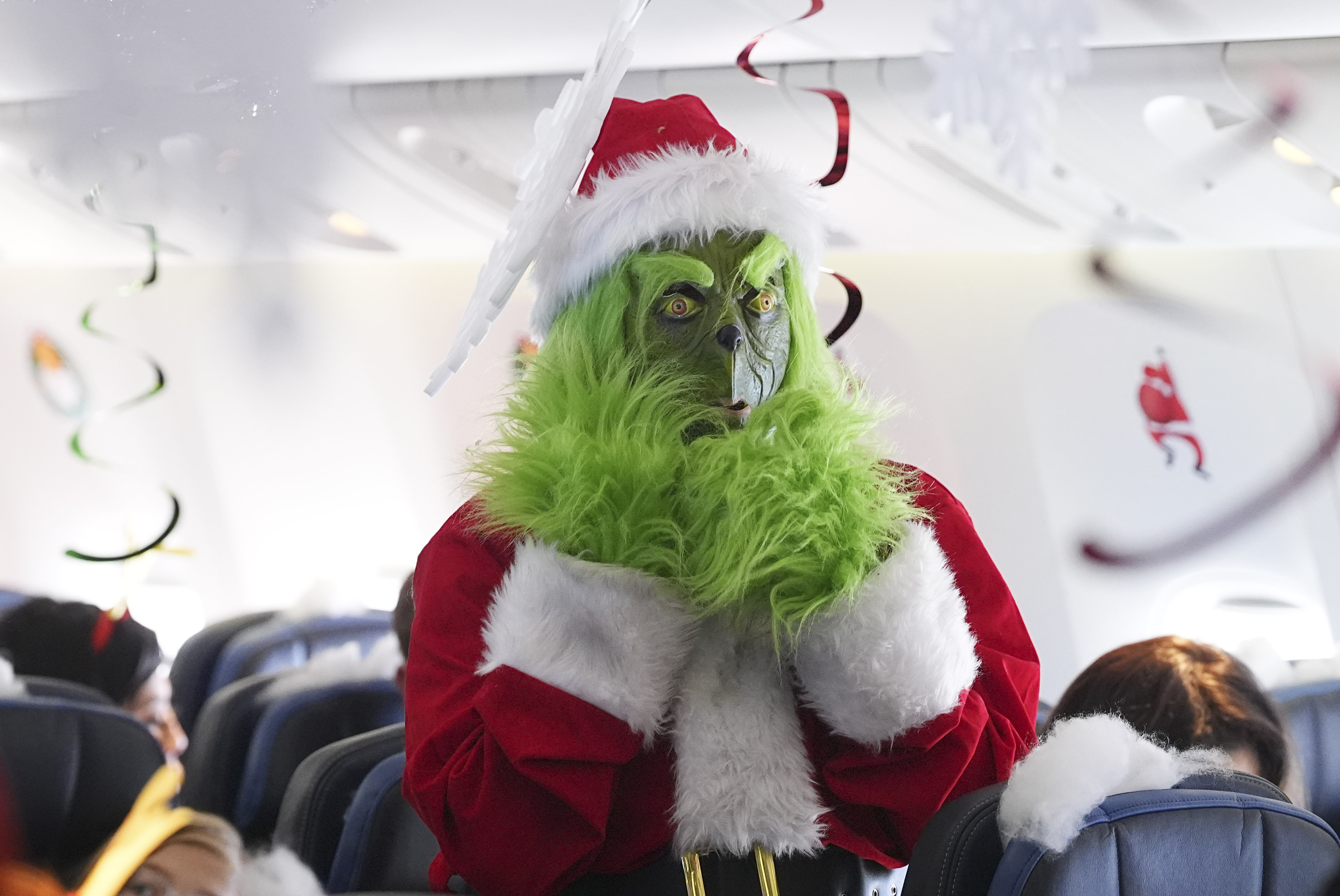 Dressed in a Grinch costume, a flight attendant entertains passengers during the United Airlines annual "fantasy flight" to a fictional North Pole at Denver International Airport, Saturday, Dec. 14, 2024, in Denver. (AP Photo/David Zalubowski)