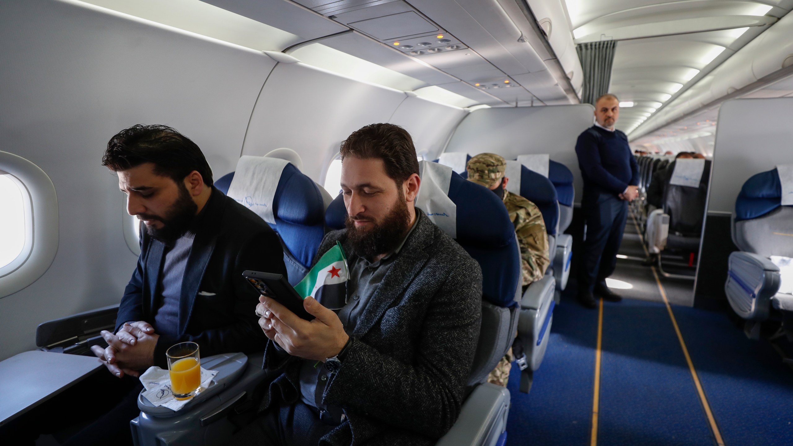 A man with a Syrian "revolutionary" flag sits inside a Syrian Air airplane ahead of take-off as the airport reopens for internal flights in Damascus, Syria, Wednesday, Dec. 18, 2024. (AP Photo/Omar Sanadiki)